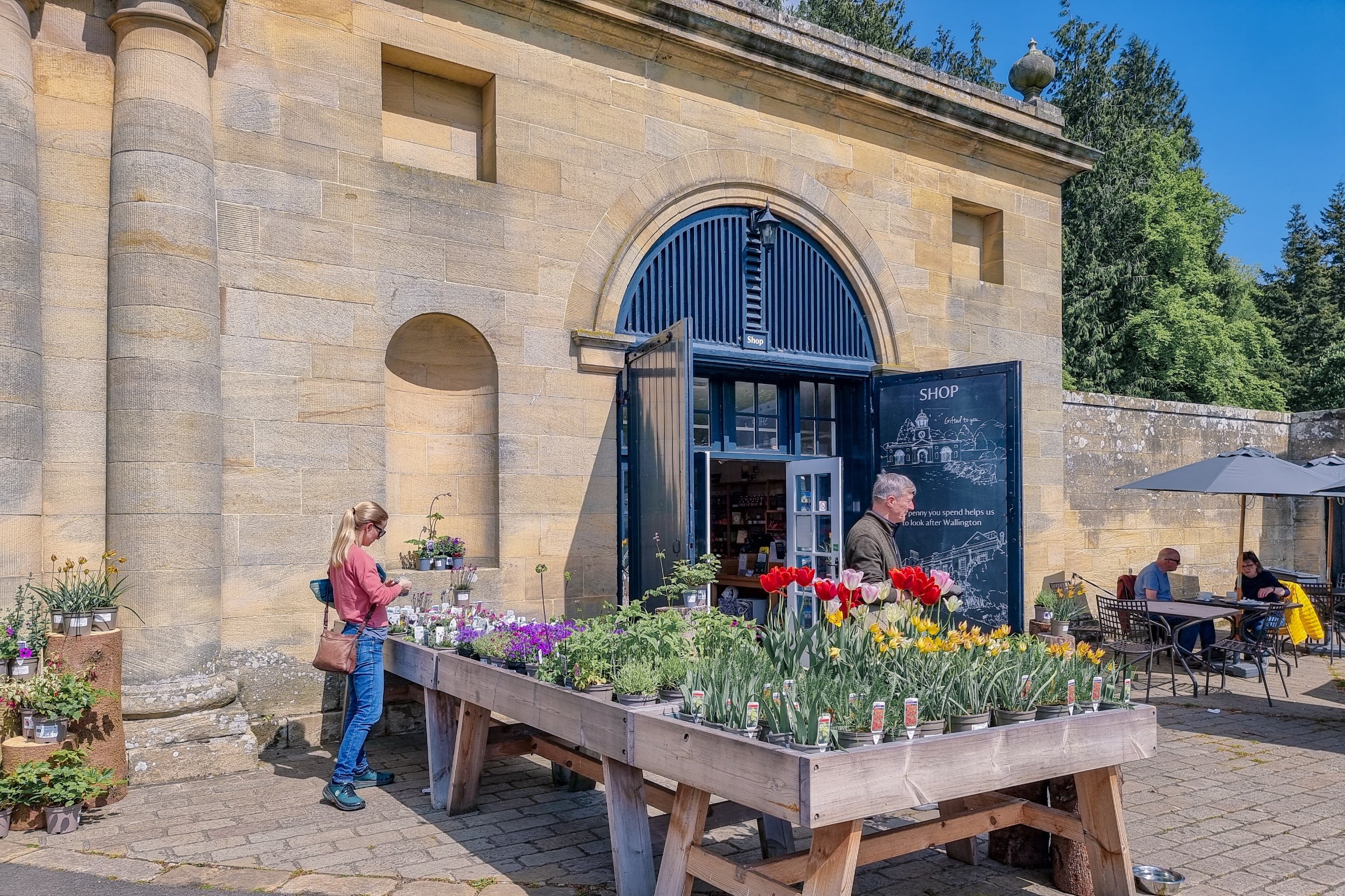 An image showing the clocktower shop with flowers for sale outside and some tables for eating food from the café.
