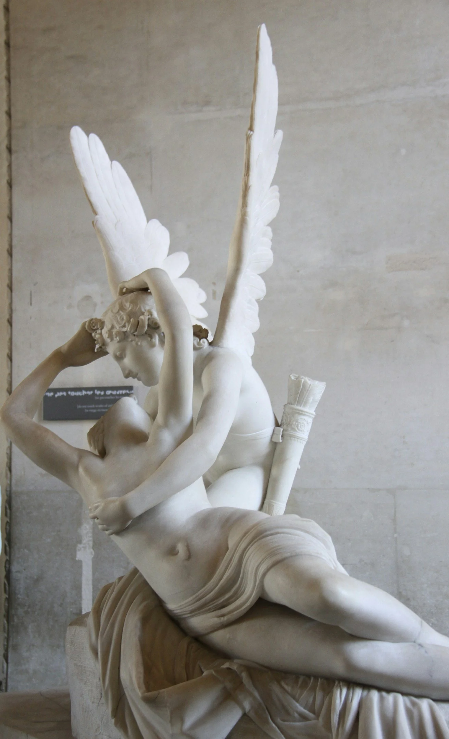 Neoclassical marble sculpture depicting a winged male figure embracing a female figure, capturing a moment of affection and tenderness in detailed artistry.