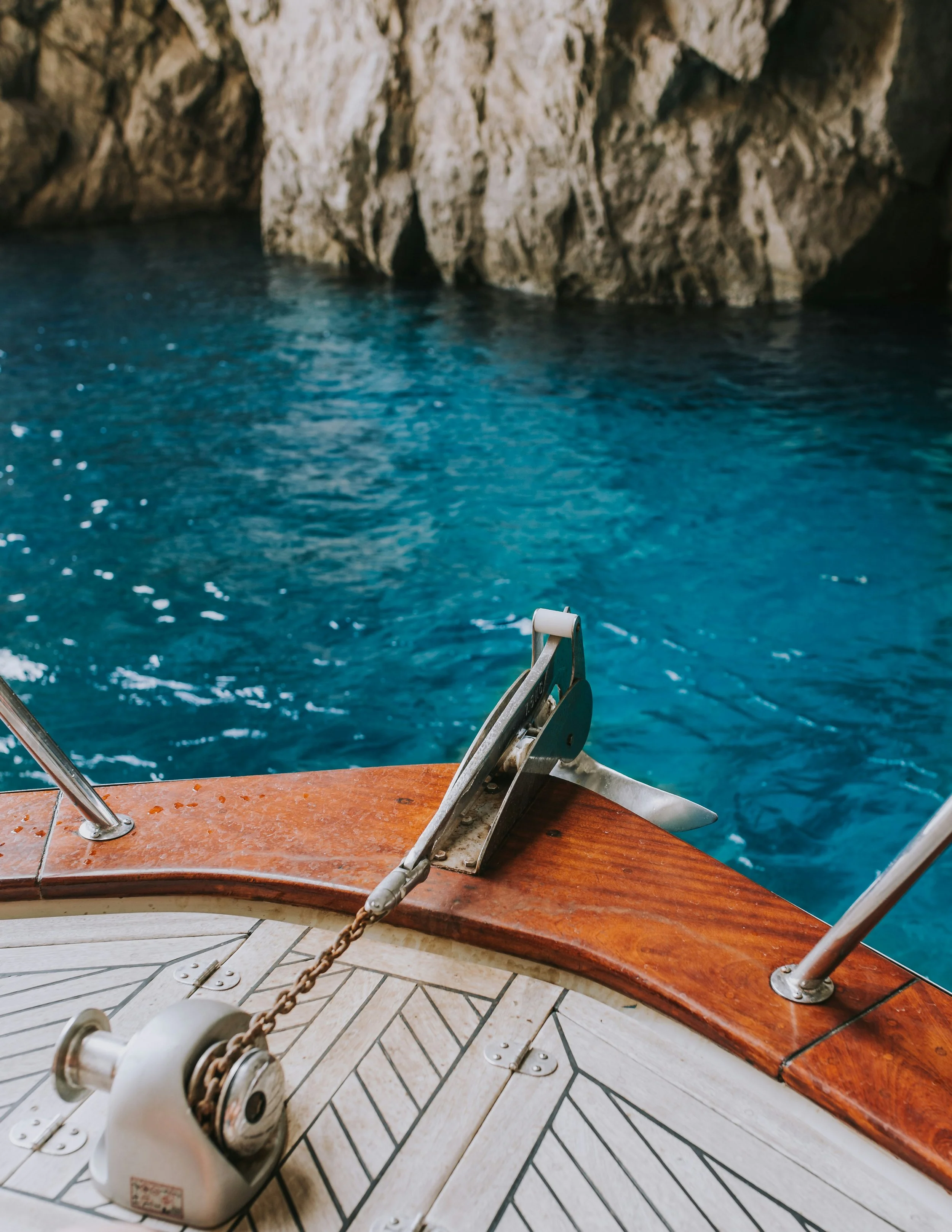 The stern of a boat in the beautiful blue waters of Capri near a rock.