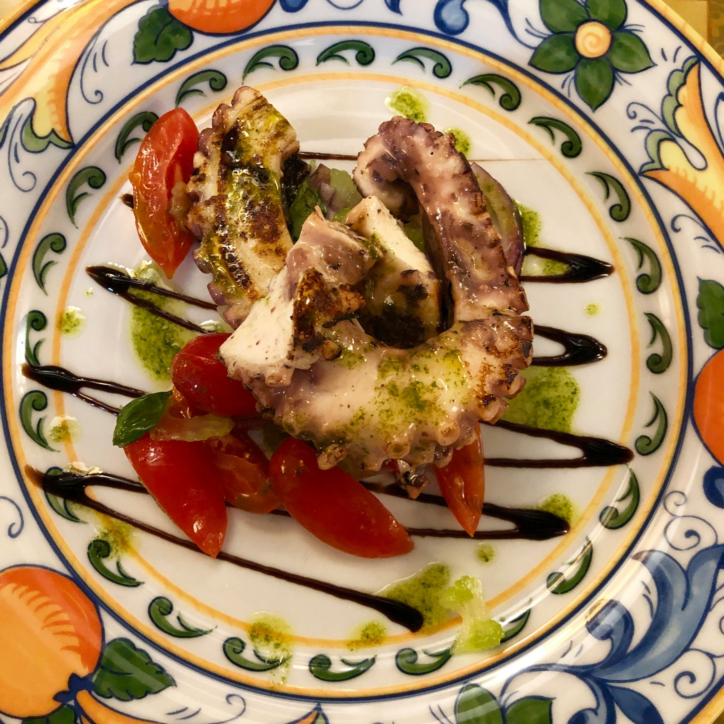 An octopus salad with tomatoes and pesto on a colourful plate