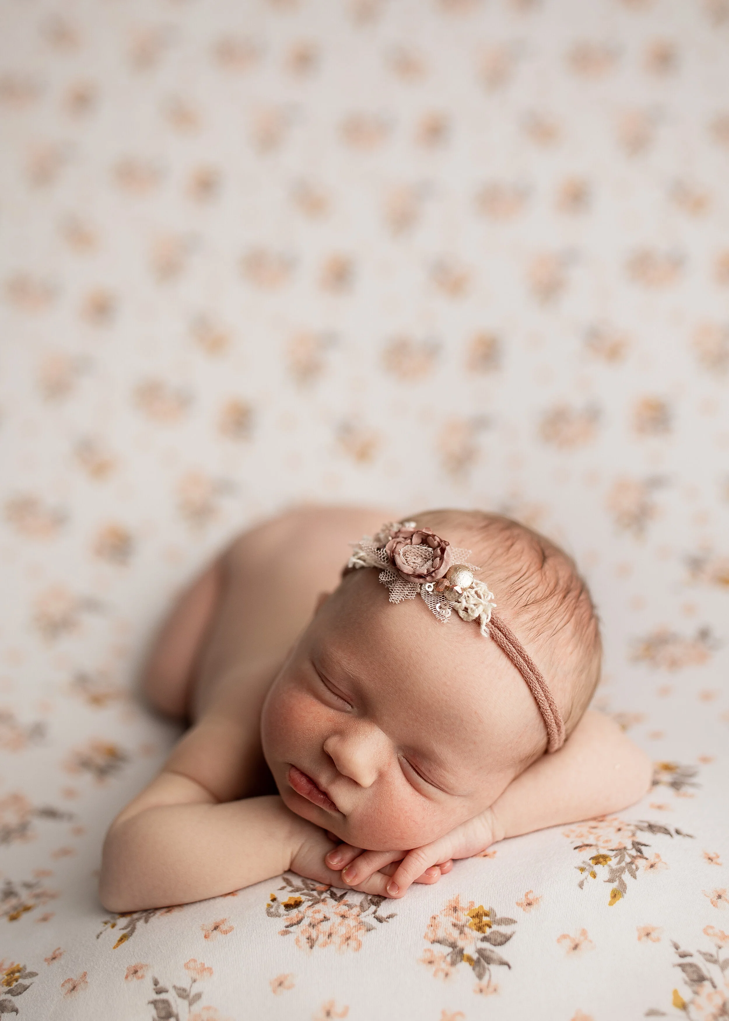 Sleeping newborn baby with floral headband on floral blanket.