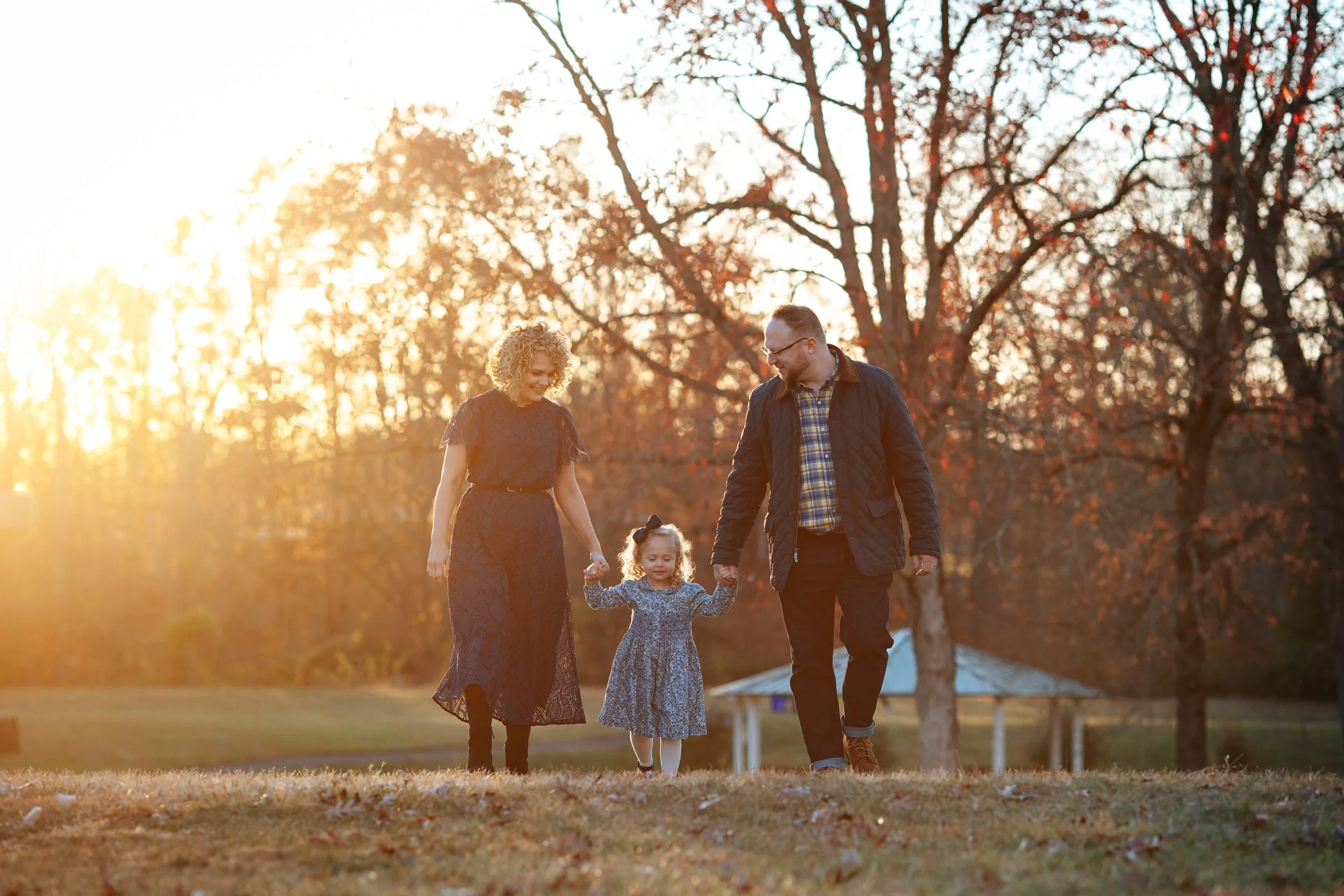 Family of 3 with a 6 year old blond girl walking towards the camera with a beautiful sunset behind them