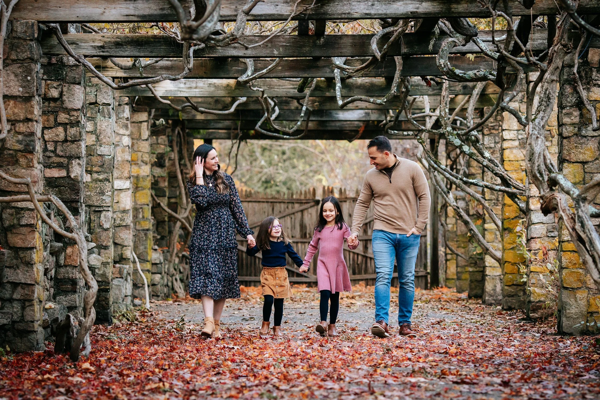 Parents with 2 girls walking holing hands talking to each other smiling in Morristown, NJ with Tamara Vaz Photography