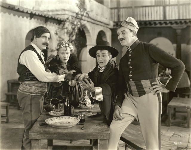 From left to right, grouped around a table in a courtyard in a scene still from the 1922 silent comedy "The Beauty Shop," are the actors James J. Corbett, Louise Fazenda, Billy B. Van, and Montagu Love. Courtesy Wisconsin Center for Film and Theater Research. Used with permission.