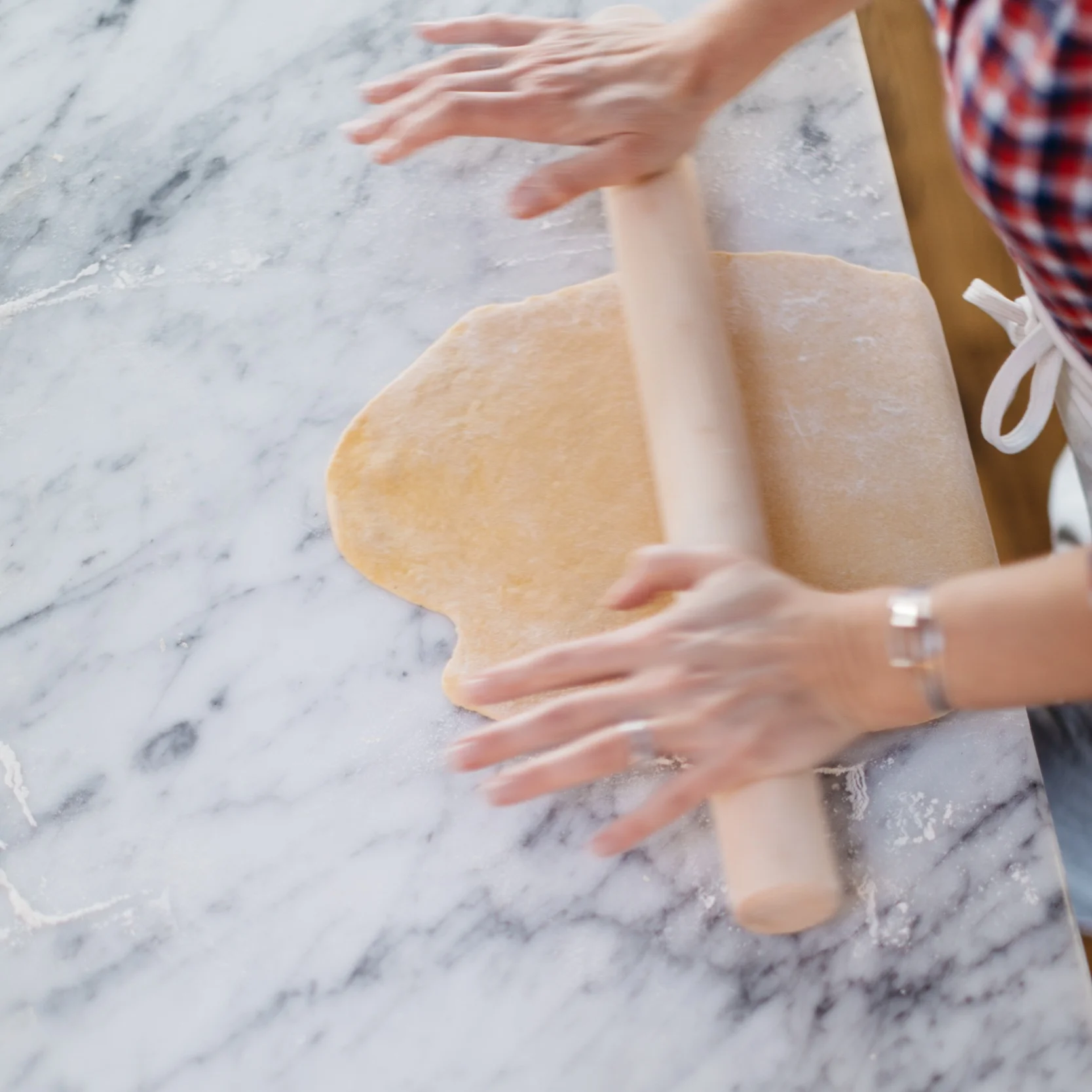 Use gravity to your advantage by hanging half the dough sheet off the front edge of your surface (at your waistline) and stretch the dough up and away with the pin. Repeat with the other end.
