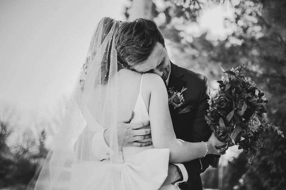 groom hugs bride tightly while crying, with his head nuzzled into her shoulder