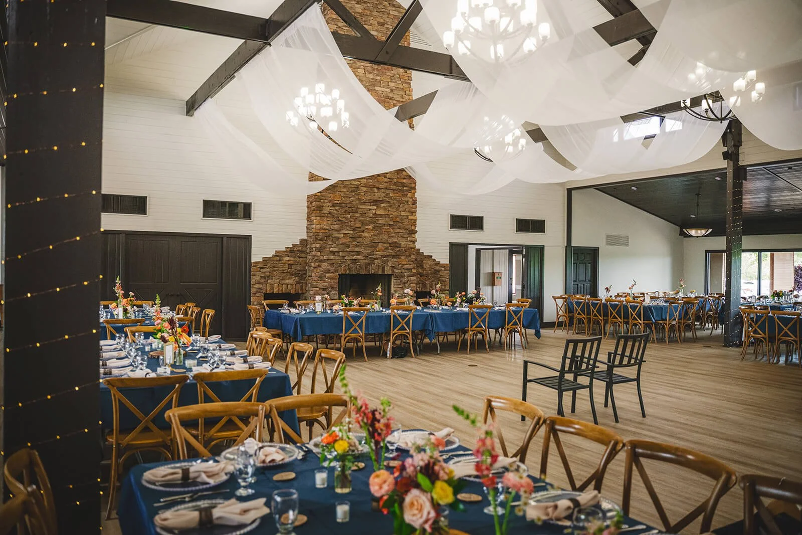 the aspen room at innsbrook resort is a white-walled room with high ceilings, a stone fireplace, and floral-adorned tables arranged throughout the space