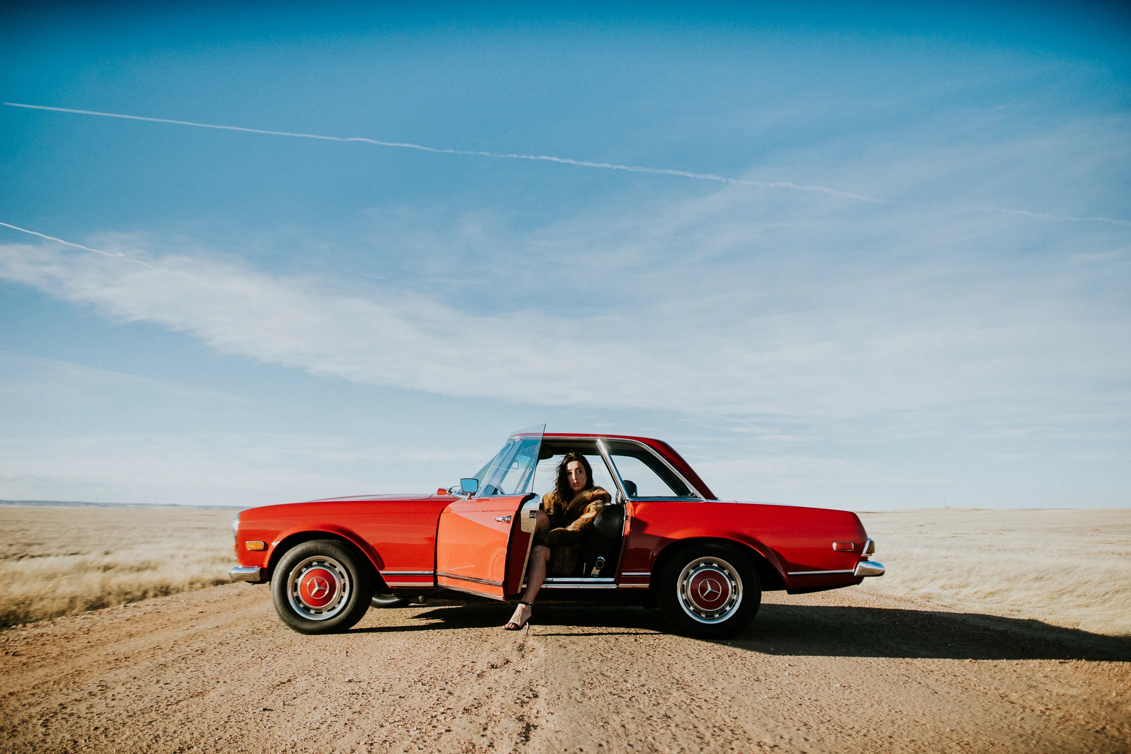 Brunette in fur coat sitting in the front seat of a classic Mercedes in rural Colorado.