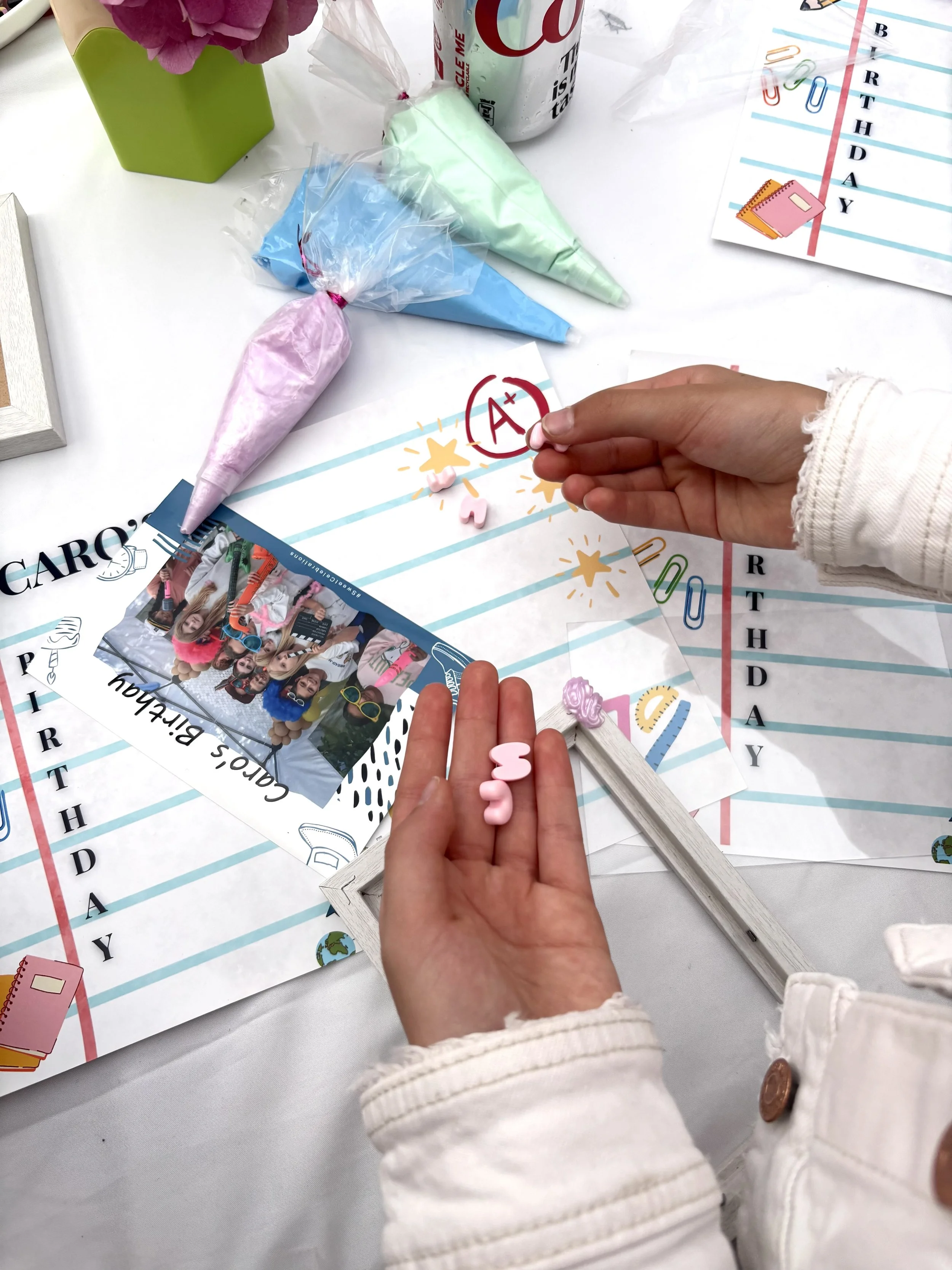 Birthday celebration scene with decorations, pink and blue party cones, and person marking an A+ grade on a birthday chart.