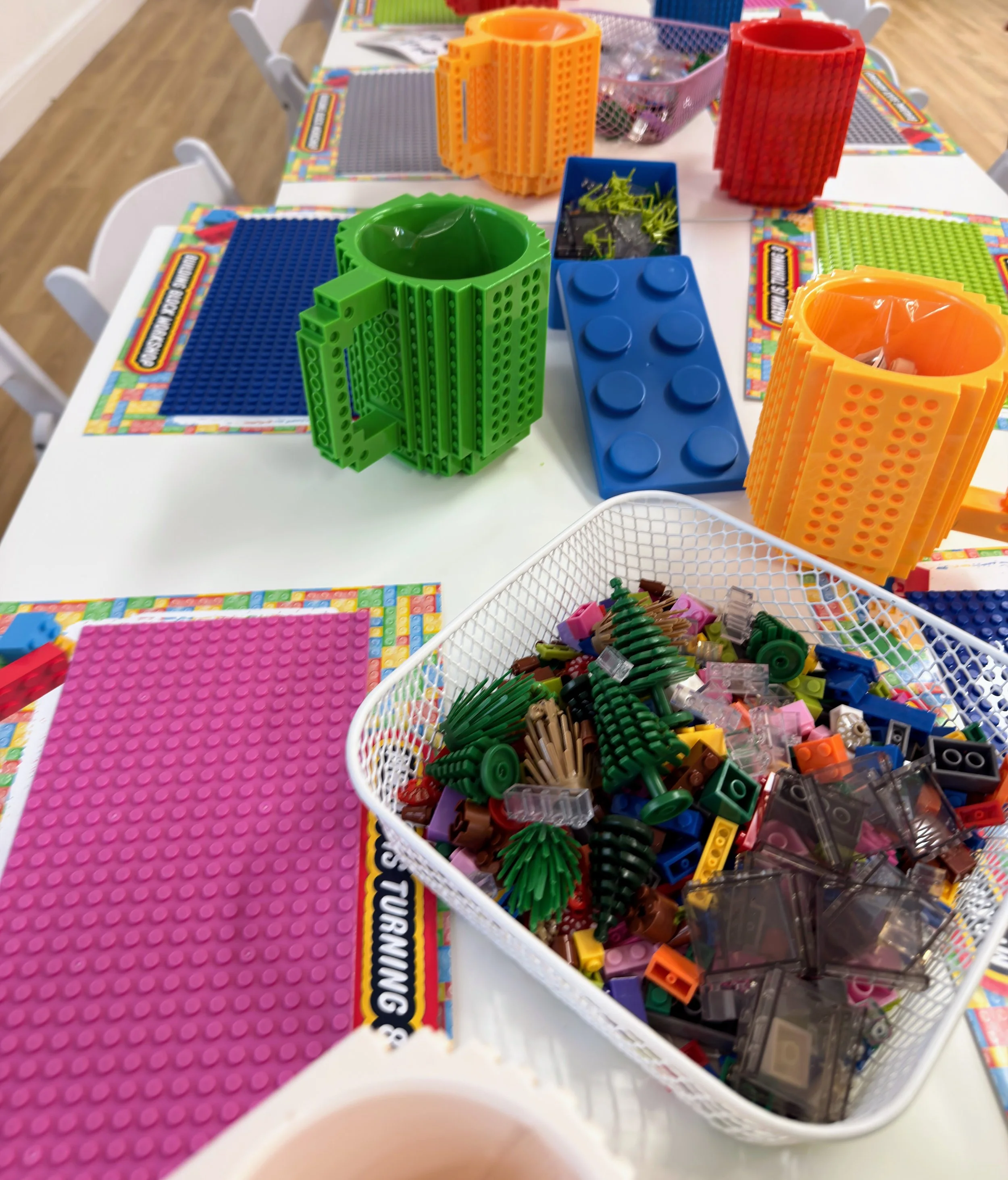 Brick Master LEGO building table for kids’ parties and workshops, featuring colorful LEGO baseplates, oversized LEGO-style brick cups, and bins of assorted LEGO bricks for creative play, STEM learning, birthday parties, and group building activities.