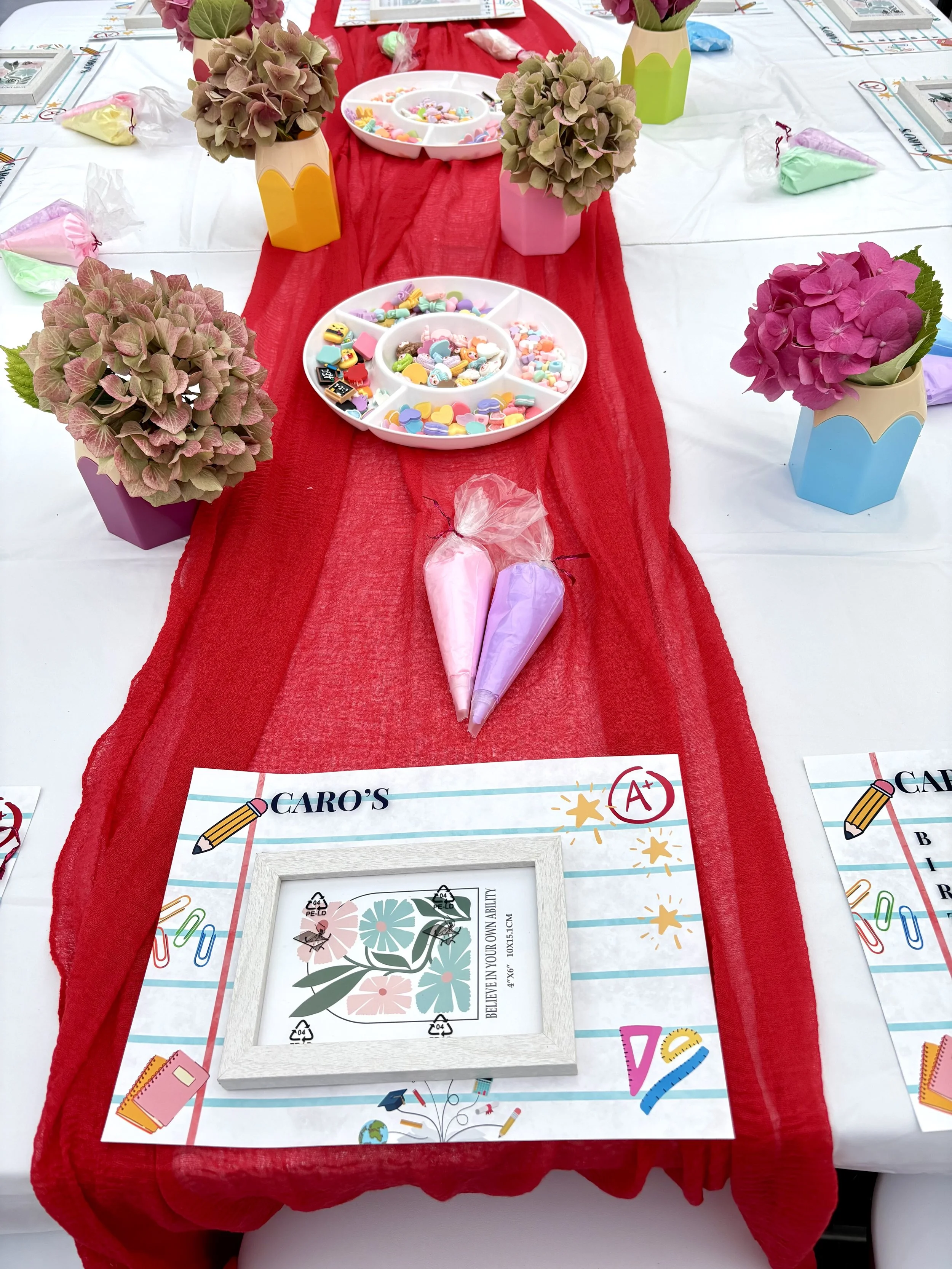 Decorated table at a birthday celebration with pink and purple hydrangea flowers, birthday hats resembling ice cream cones, and colorful party favors.