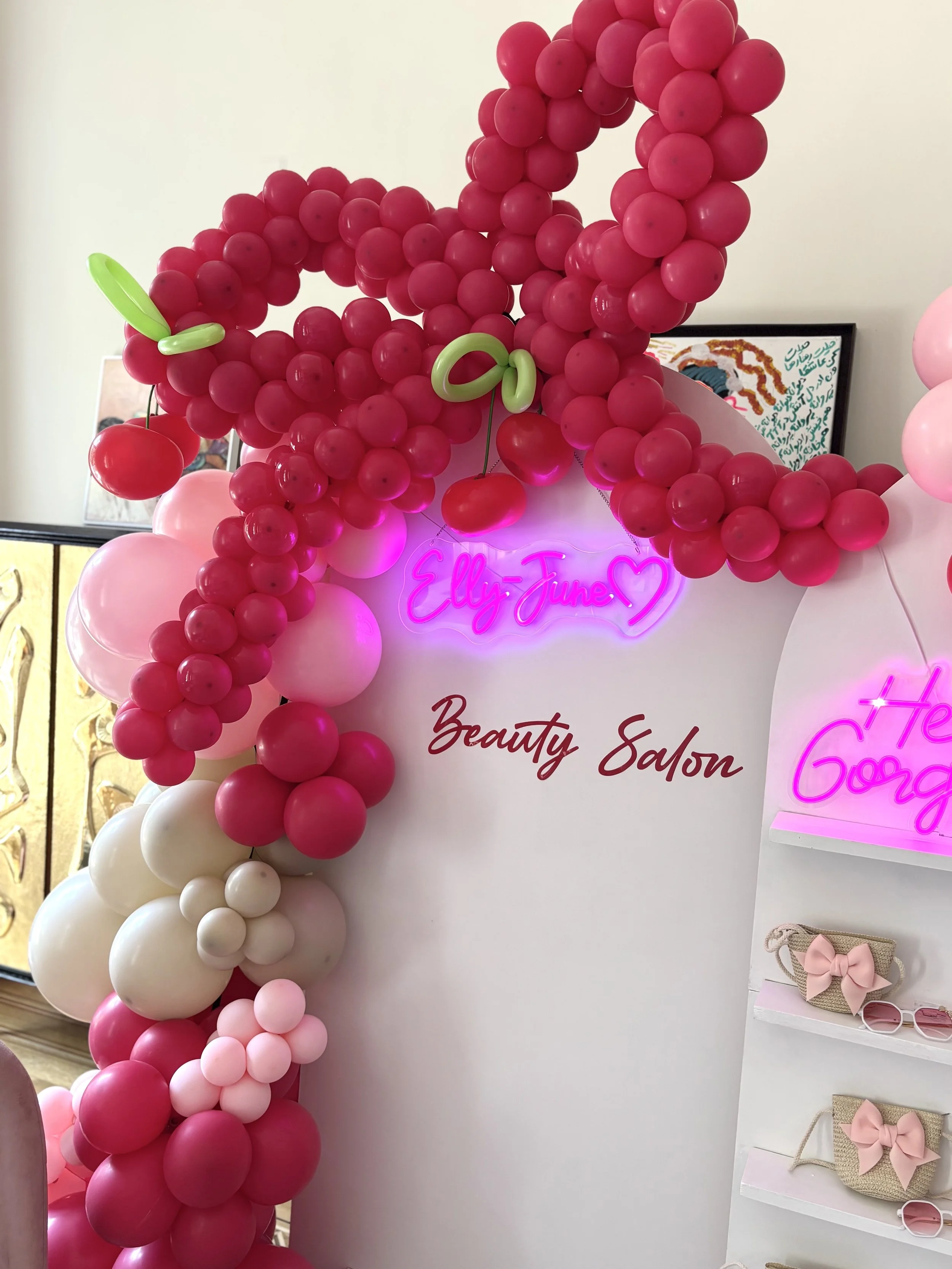 Decorative balloon arrangement with pink, white, and red balloons, with neon signs and a sign reading 'Beauty Salon'.