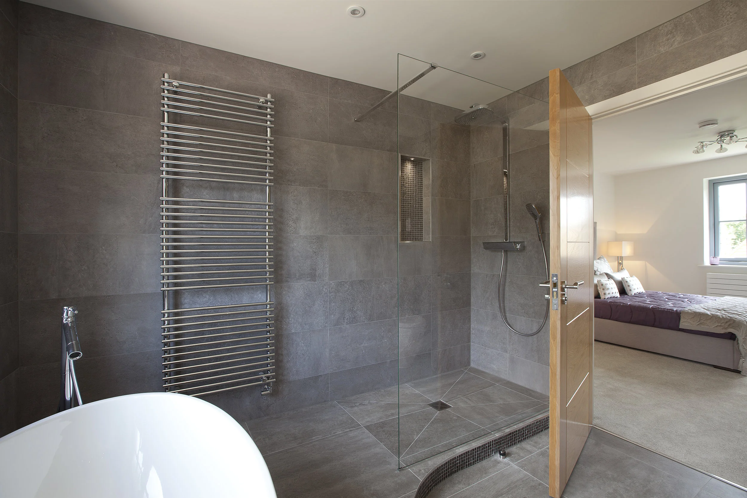 Modern wet room with curved detail step and freestanding bath. Wall and floor tiling uses Porcelanosa® grey slate porcelain.