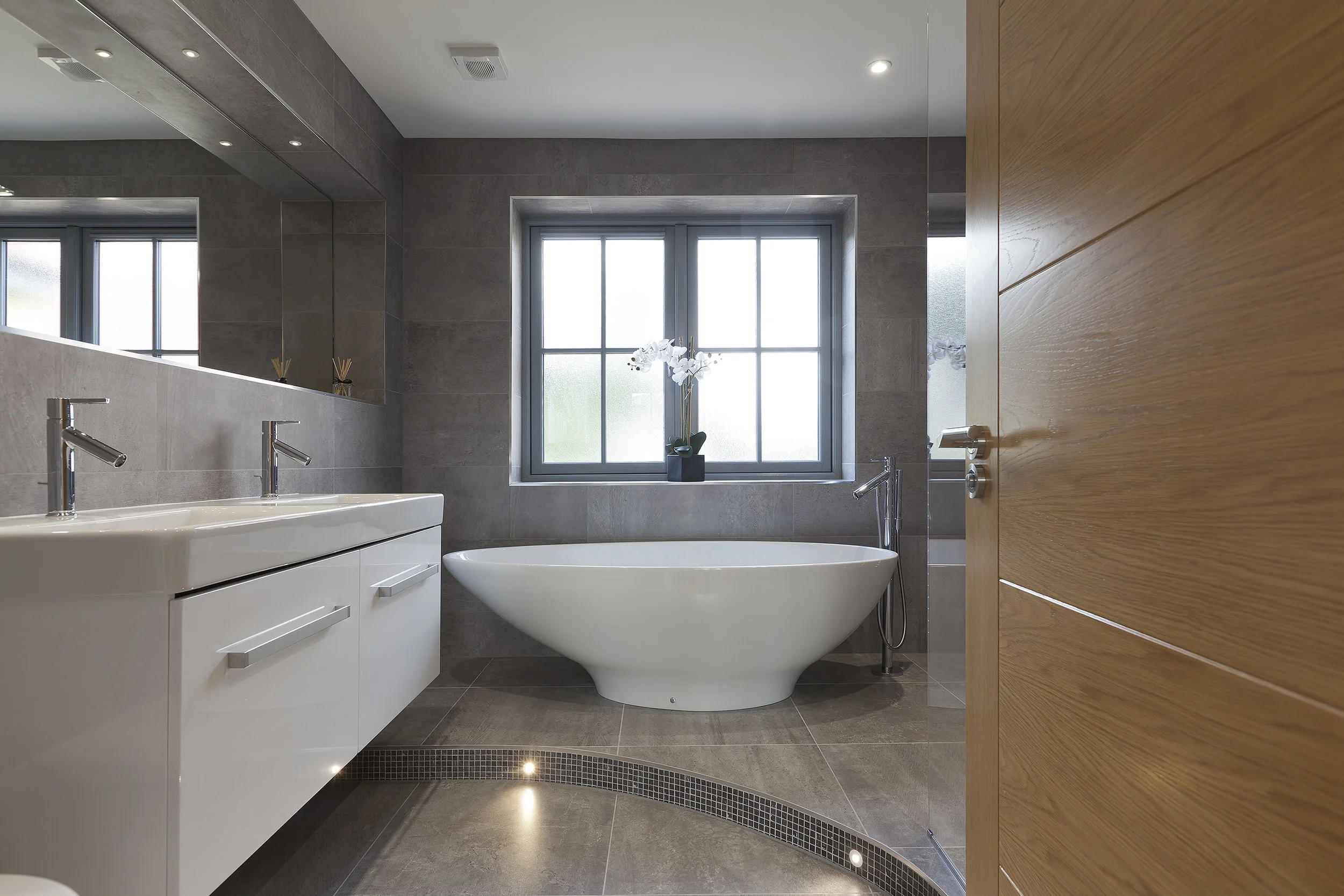 View into the wet room, highlighting curved detail step, freestanding bath and mirrored niche.