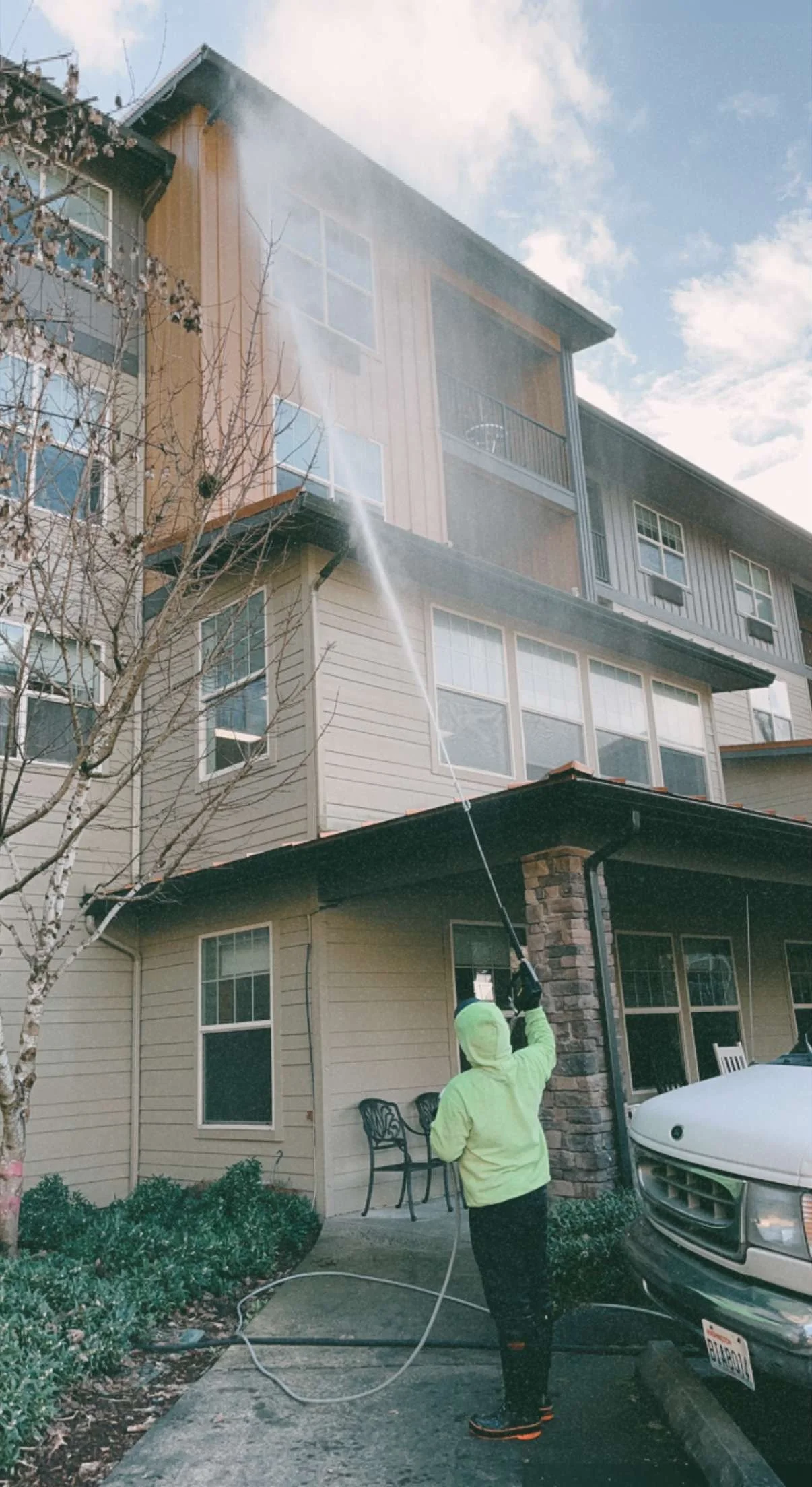 Person in a yellow jacket power washing the exterior of a multi-story apartment building