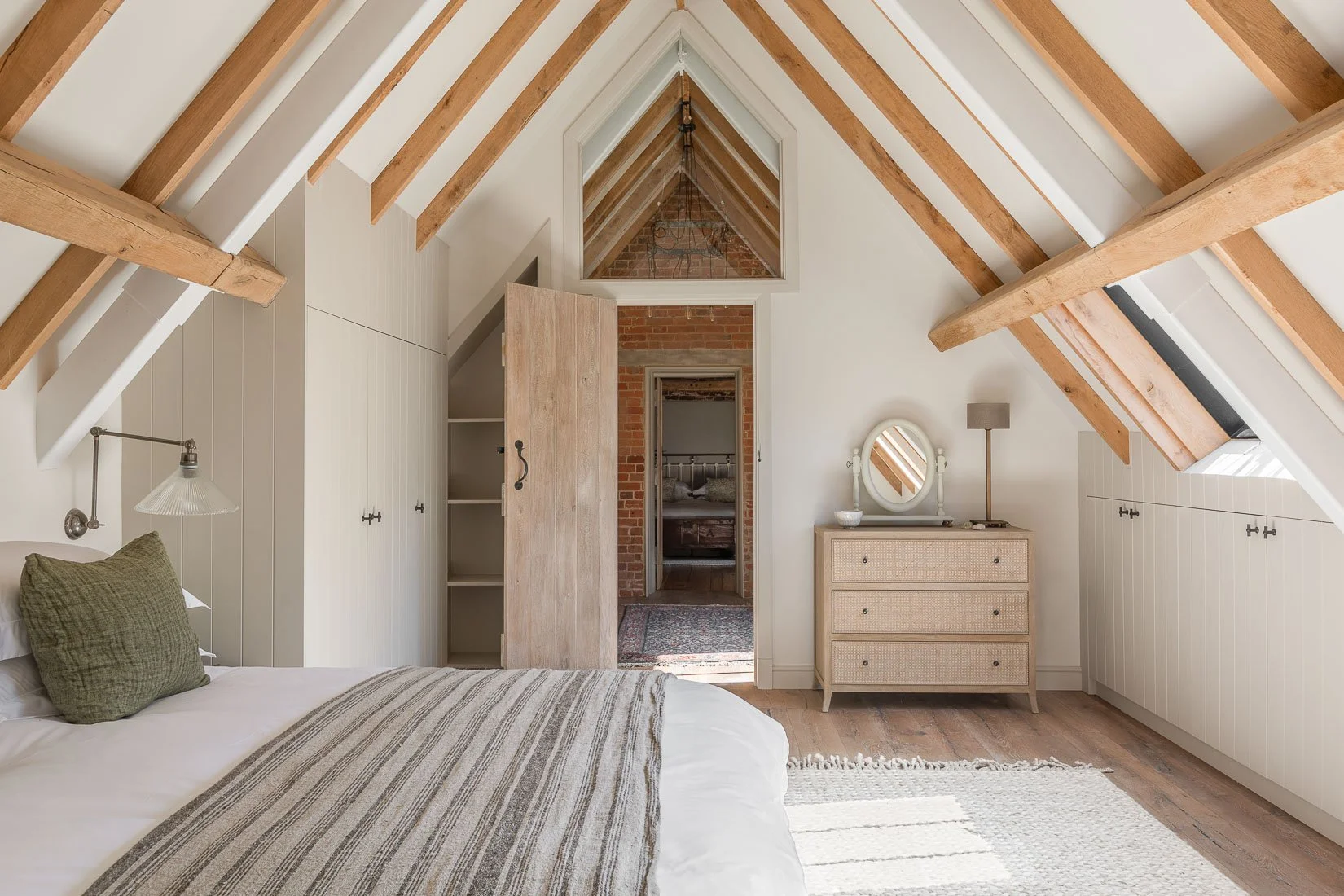 Period coach house outbuilding conversion restoration bright and airy loft bedroom with natural rug, exposed beams, fitted wardrobes and eaves storage.