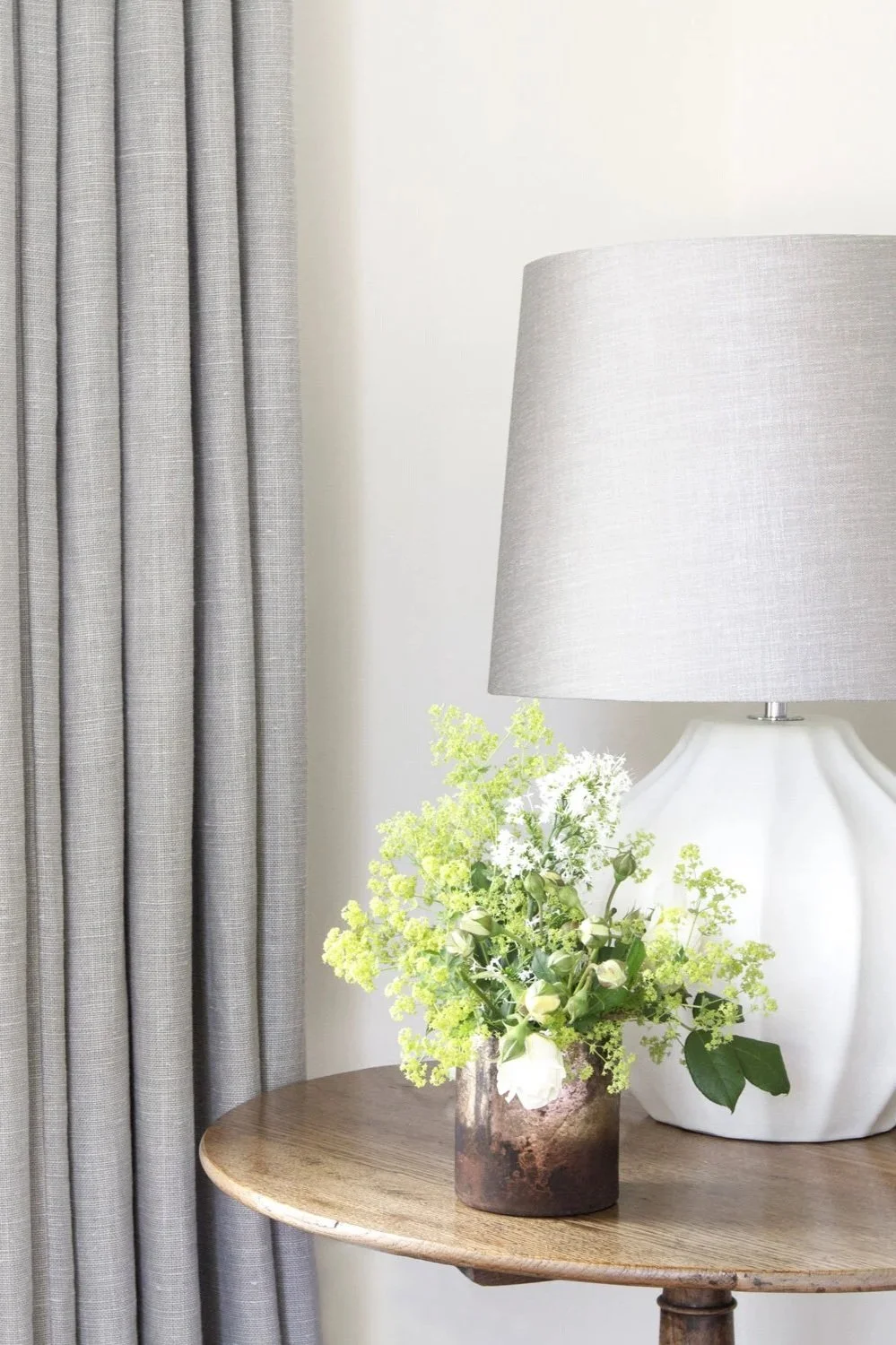 Bright and airy living room with an antique side table, table lamp, and blue grey linen curtains.