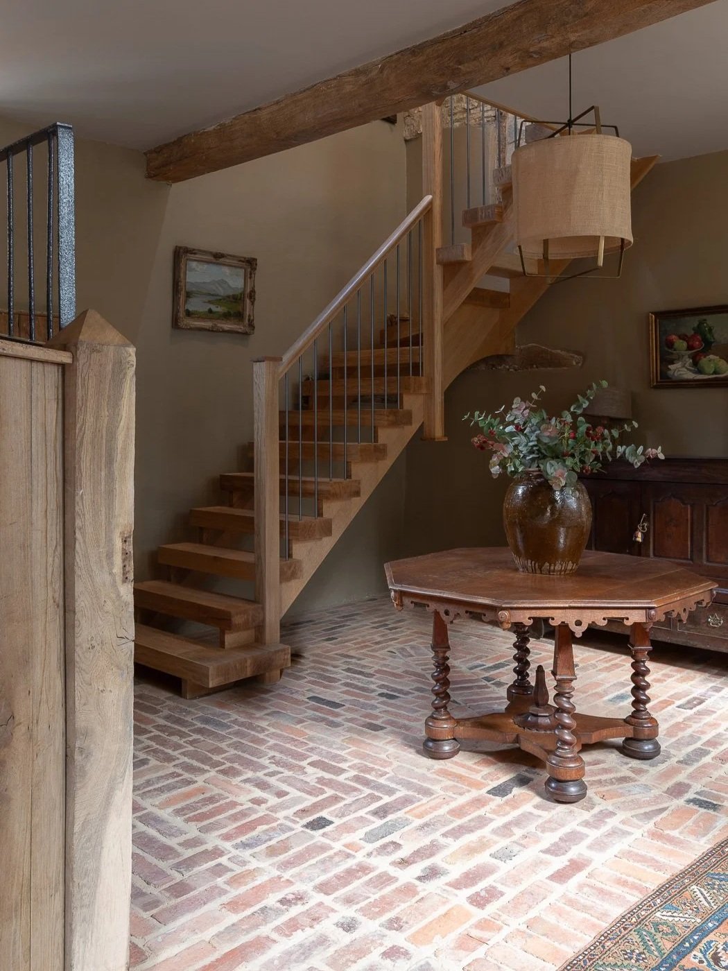 Period stables barn conversion restoration entrance hall with wooden staircase, original brick floor and antique rug.