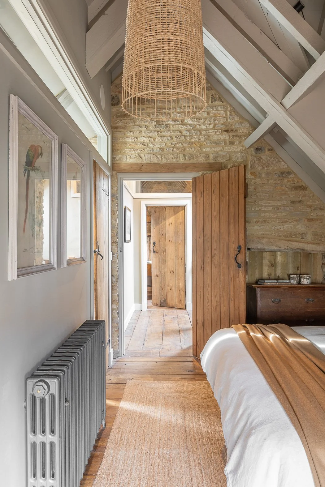 Period stables barn conversion restoration loft bedroom with exposed beams, rattan pendant lights, jute rug and exposed stone walls.