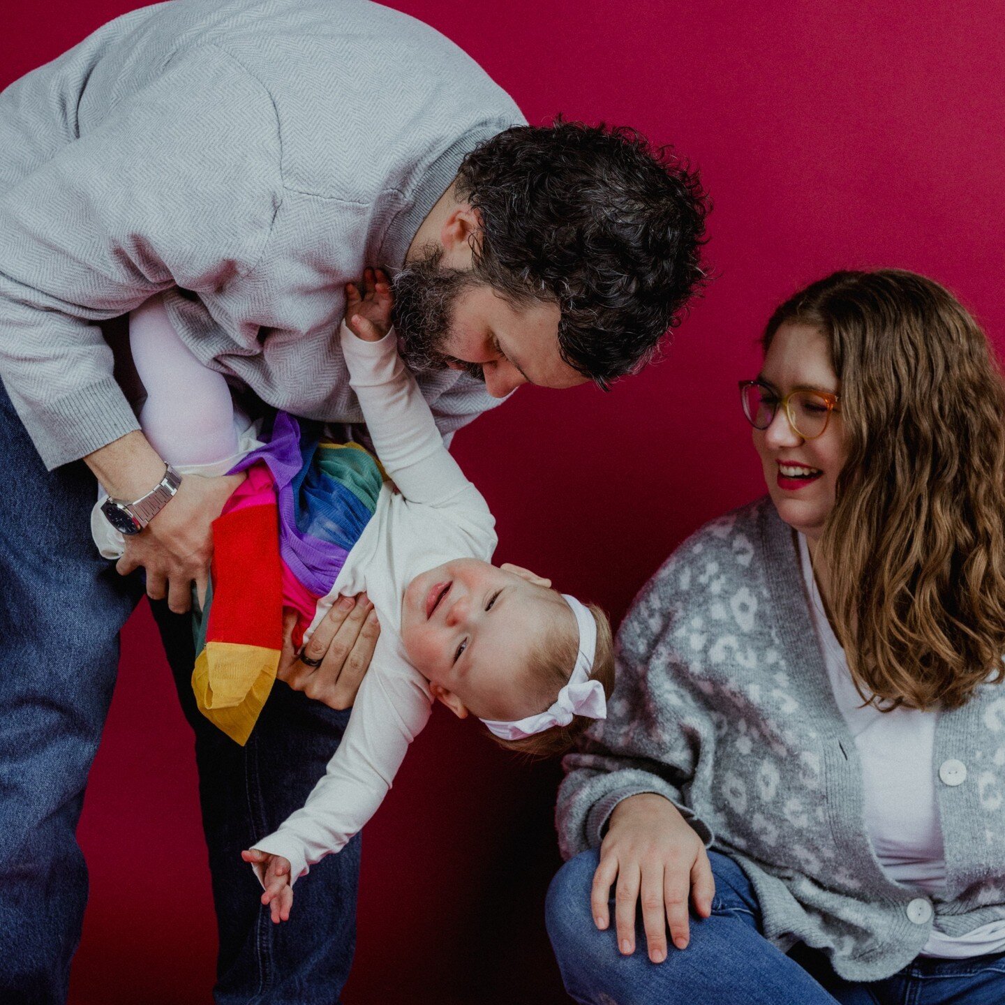 This little one year birthday session was a blast! I'd love to do more family sessions at the studio! 🤩
.
.
.
.
.
[Image Description: A white man with short dark hair and a beard is holding a one year old baby in a rainbow dress and white bow. She i