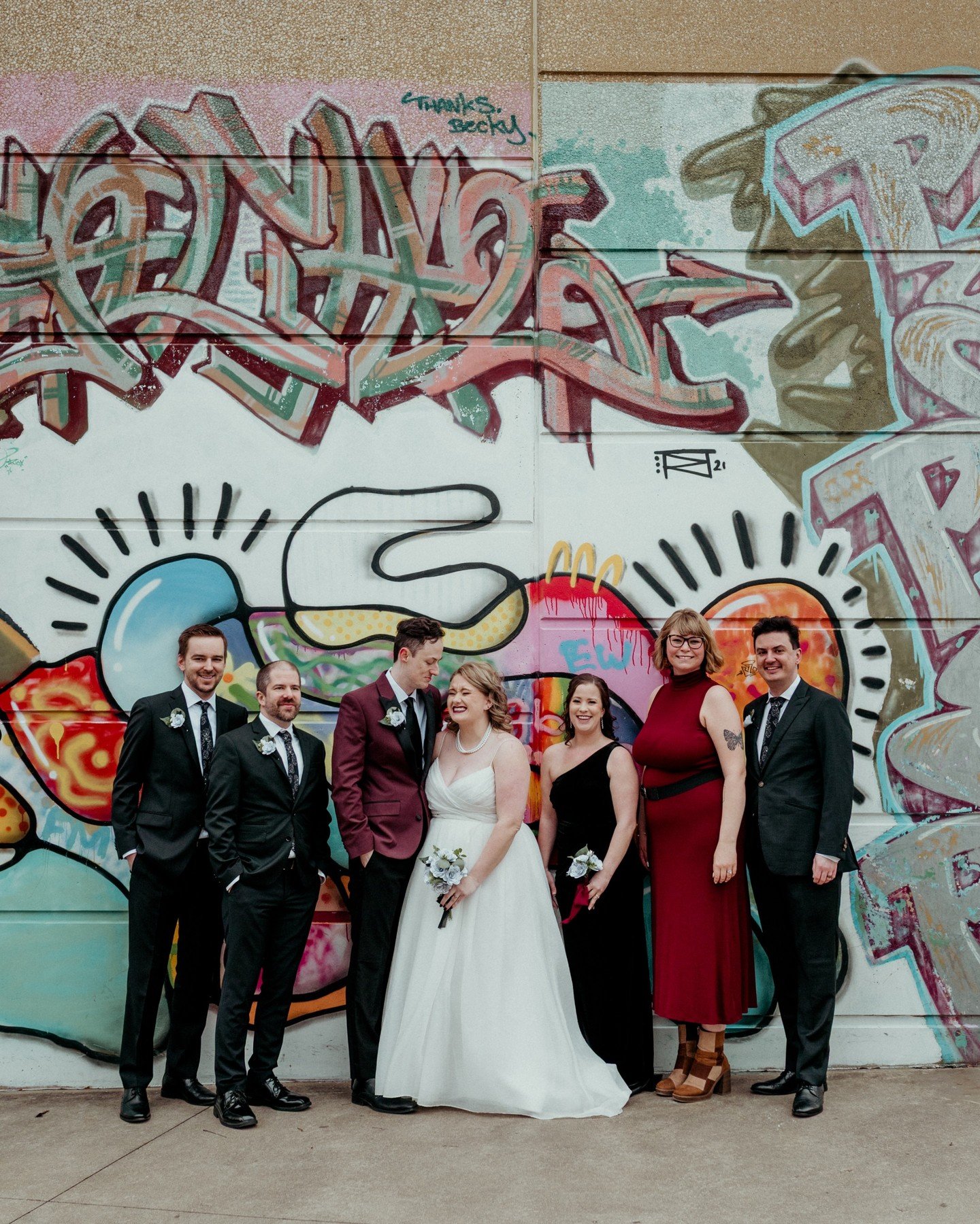 I love a good graffiti wall or mural wall, don't you? 😍
.
.
.
.
.
[Image Description: A white woman with blonde medium length hair in a white wedding gown is holding a bouquet of book page flowers laughing next to a white man with brown hair wearing
