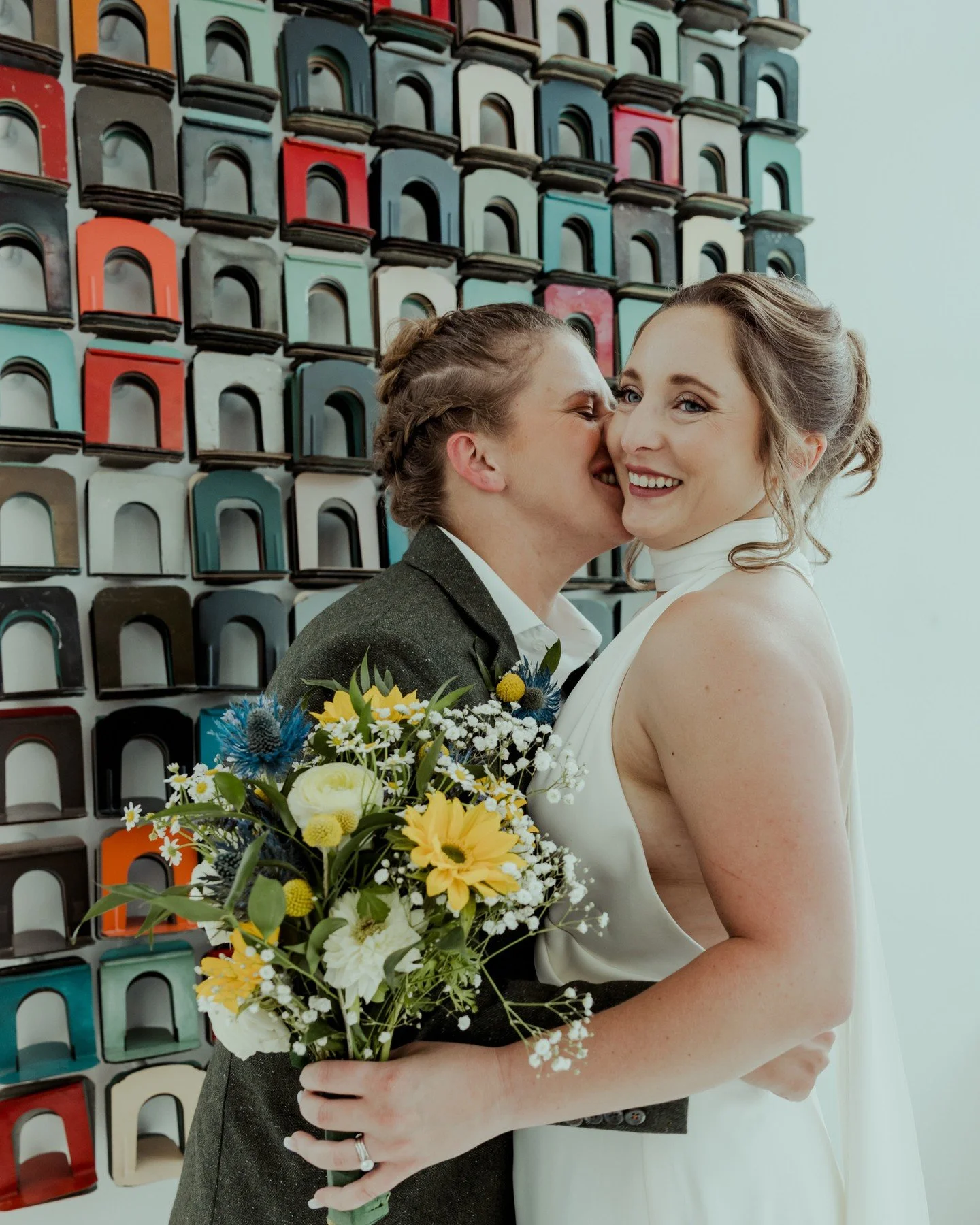 Any guesses where this was taken??? Hint: It's one of my favorite spots downtown for weddings!
.
.
.
.
.
.
[Image Description: A white woman with a braided up-do and dark olive green wool suit is kissing a white woman with an up-do wearing a white ha