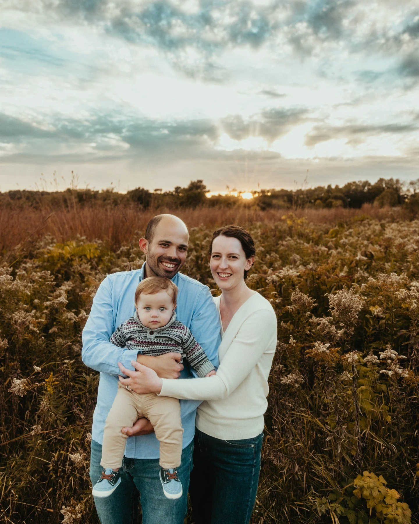 Okay, but this adorable family though.... 🥹
.
.
.
.
.
.
[Image Description: A man with medium-light skin tone and black hair &amp; beard wearing a blue dress shirt is holding a white infant with blond hair. They are next to a white woman with long d