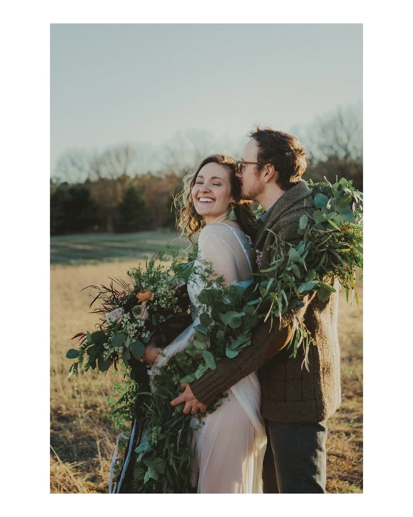 Have I mentioned how much I love floral garlands??? 🤣❤️🤩
.
.
.
.
.
.
.
[Image Description: A white woman with long light brown hair is wearing a boho wedding dress and is holding a large bouquet of mostly greenery. Her husband, a white man with sho