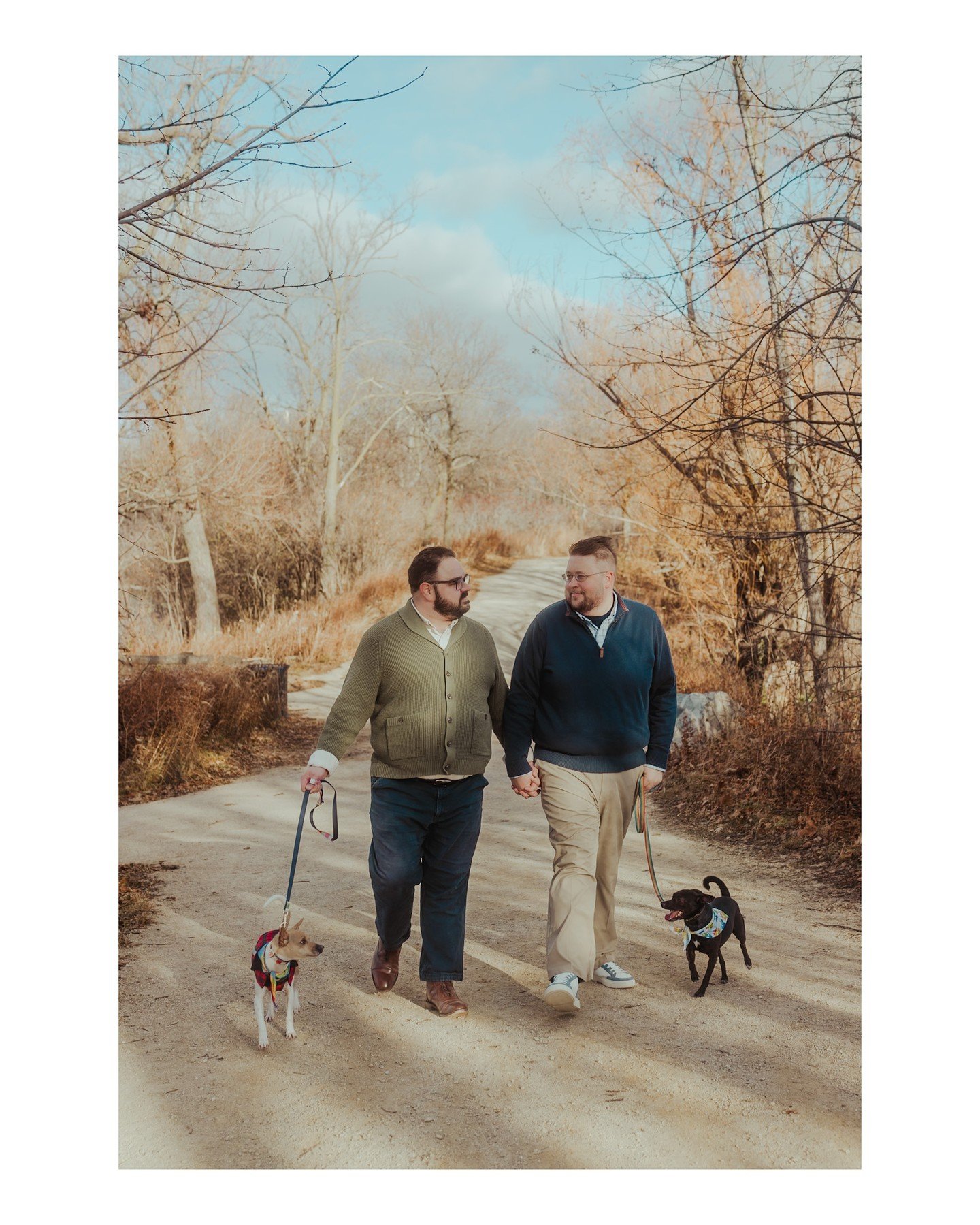 We're so excited to celebrate David + Alex's wedding next weekend!!! 🥳🥰
.
.
.
.
.
.
[Image Description: Two men wearing a green sweater and a blue sweater are walking down a path and holding hands and smiling at each other as they walk their two do