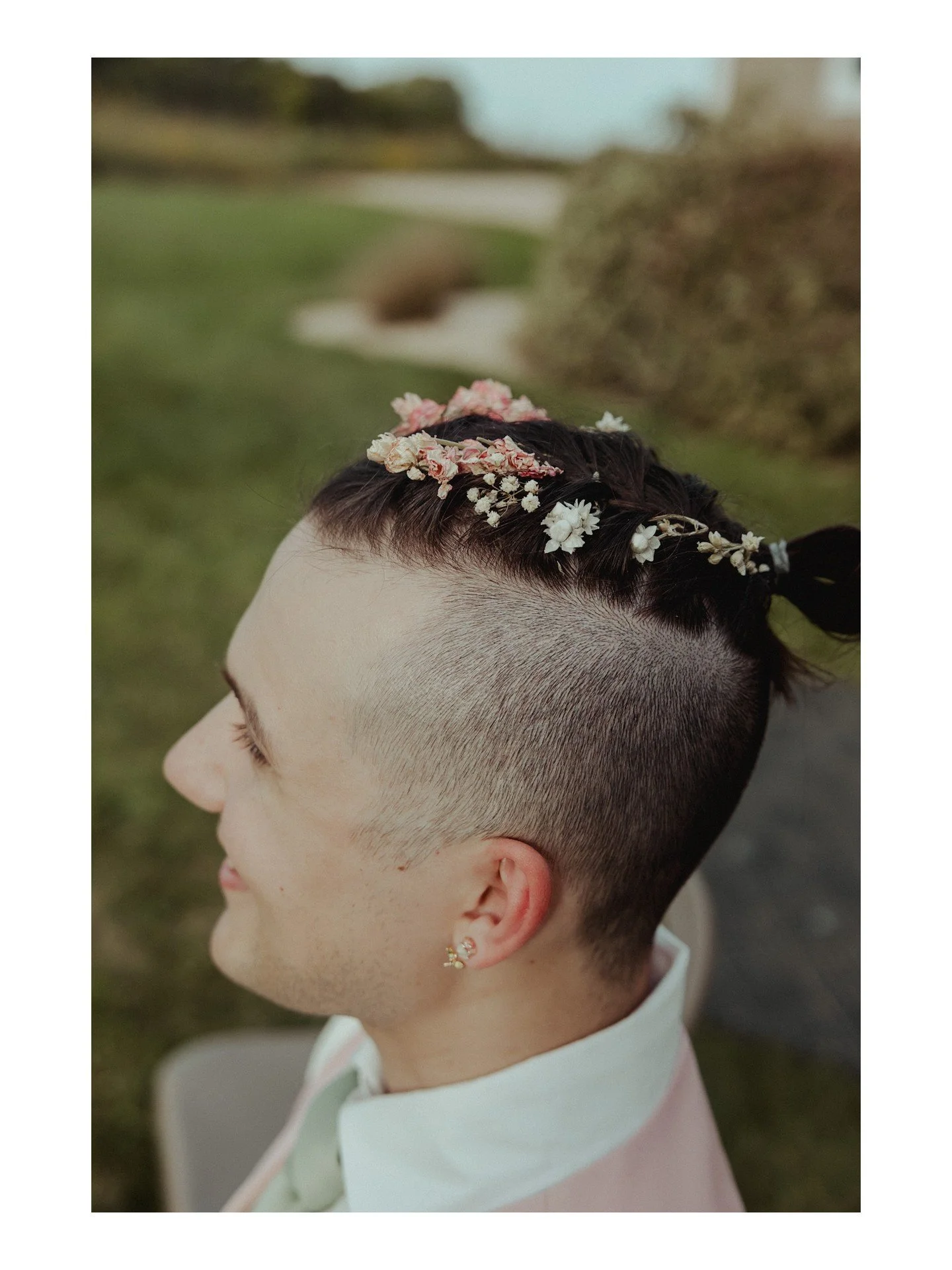 You know what I absolutely ADORE? Braided updos and floral crowns or accessories on more masc-presenting folks! Caleb (he/they) had the *perfect* stylish braided updo, complete with DIY flowers braided in, for their Hobbit-themed wedding day (more to