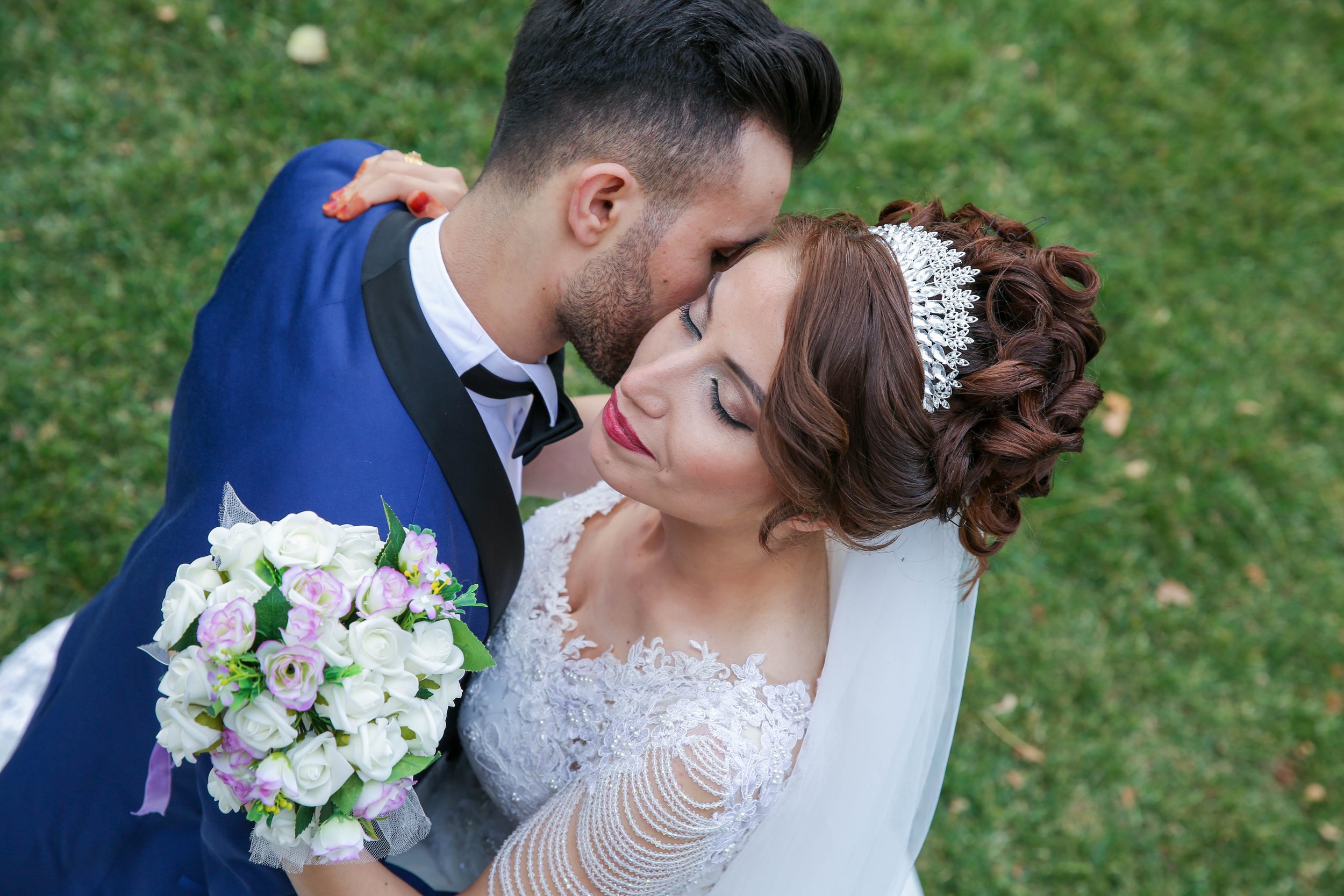 Latino wedding couple groom in blue suit and bride in white dress with boquet of white flowers kissing one another.jpg