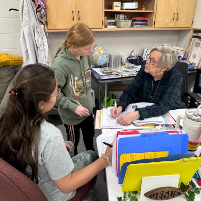 GCS approved 2 students talking with teacher at desk.png