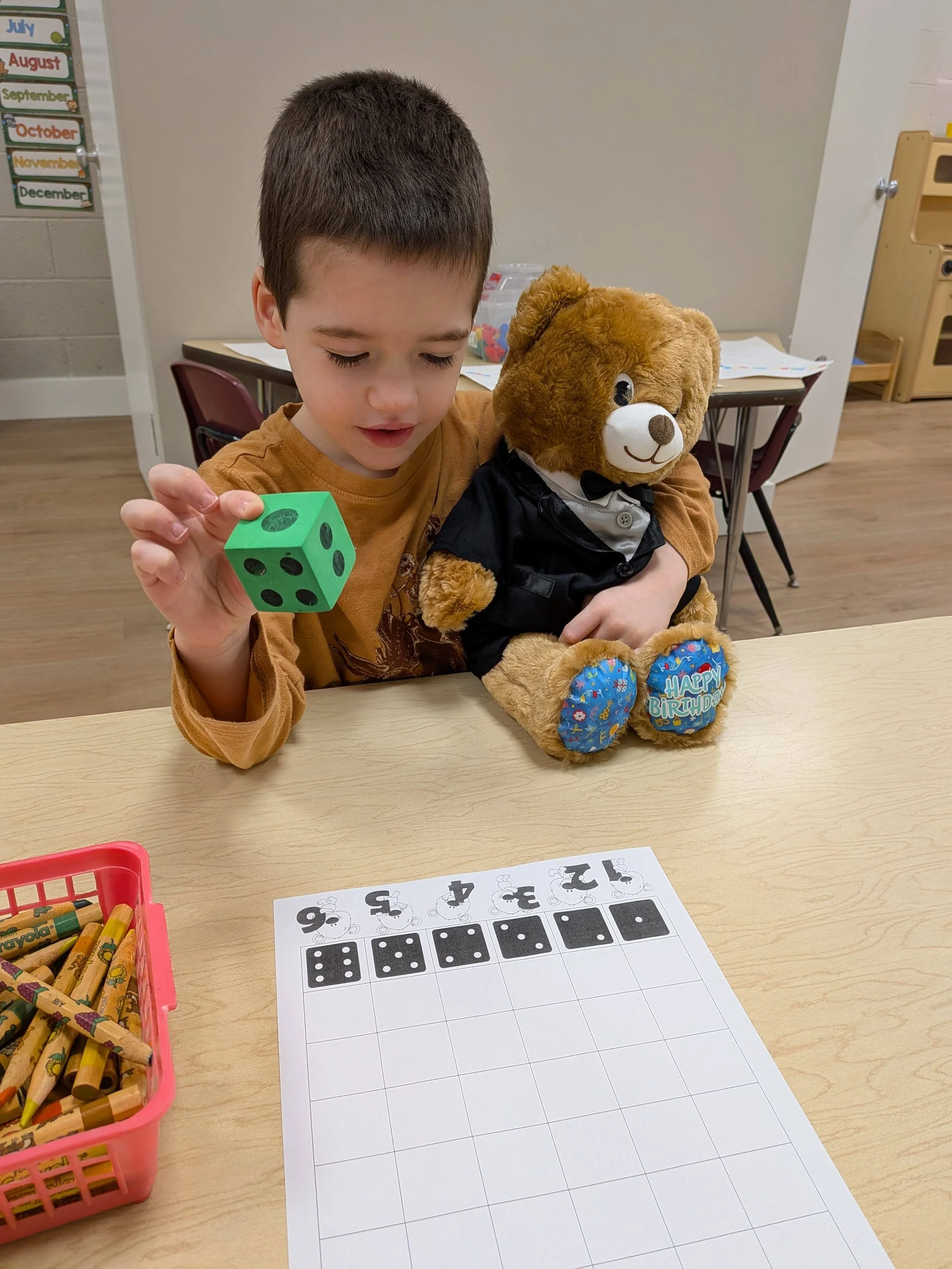 PreK student working on numbers while holding teddy bear