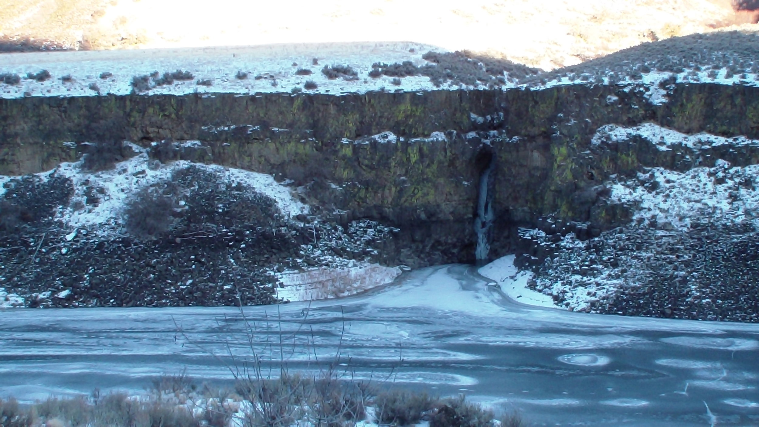 An unnamed waterfall pours into frozen Arrowrock Reservoir.