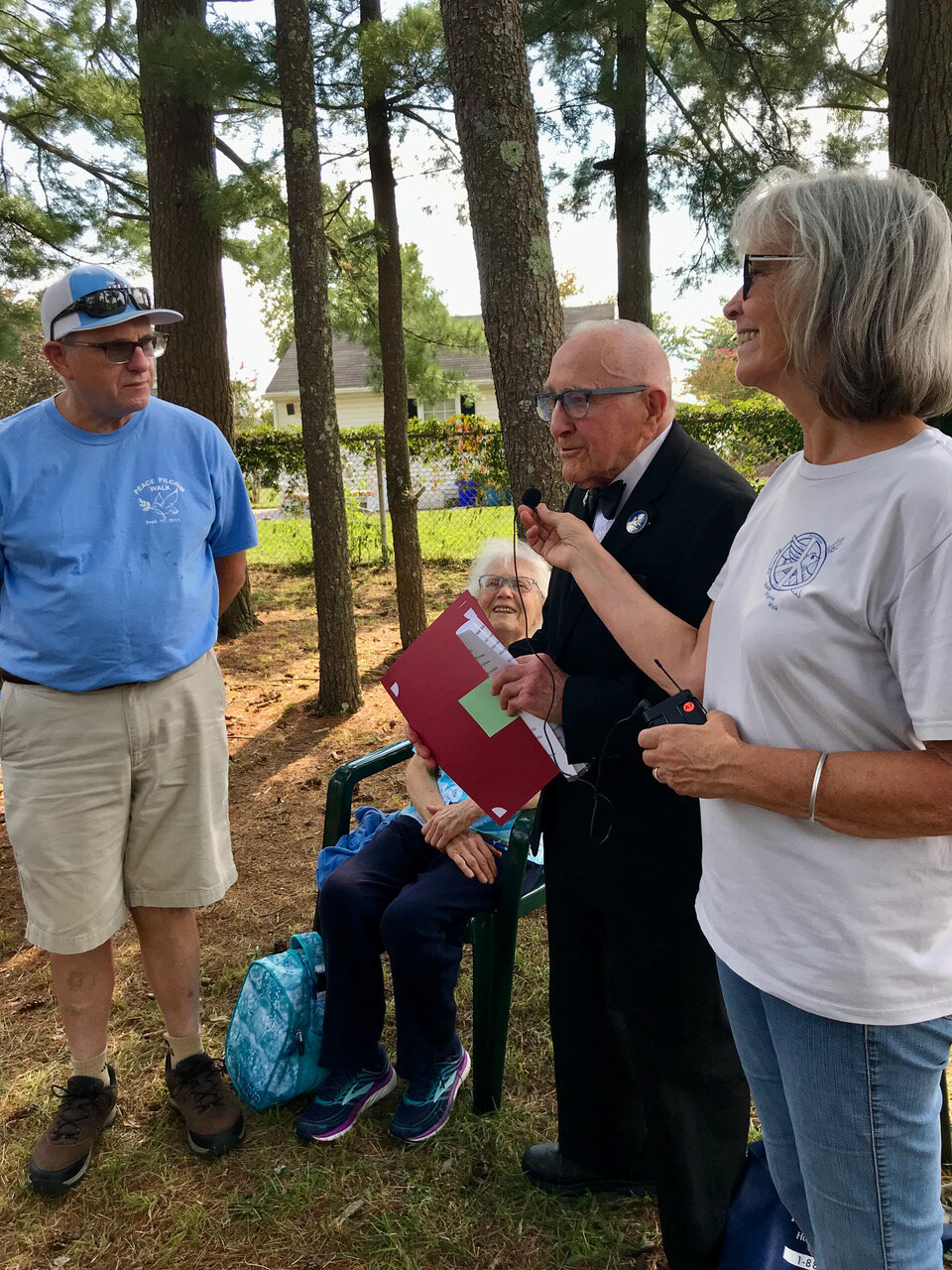  Al Shollenberger, with his wife May seated behind him, reads proclamations in honor of Helene Young, which he presented to her son Dale Young (left). FoPP Board Member Barbara Young holds a portable mic.  