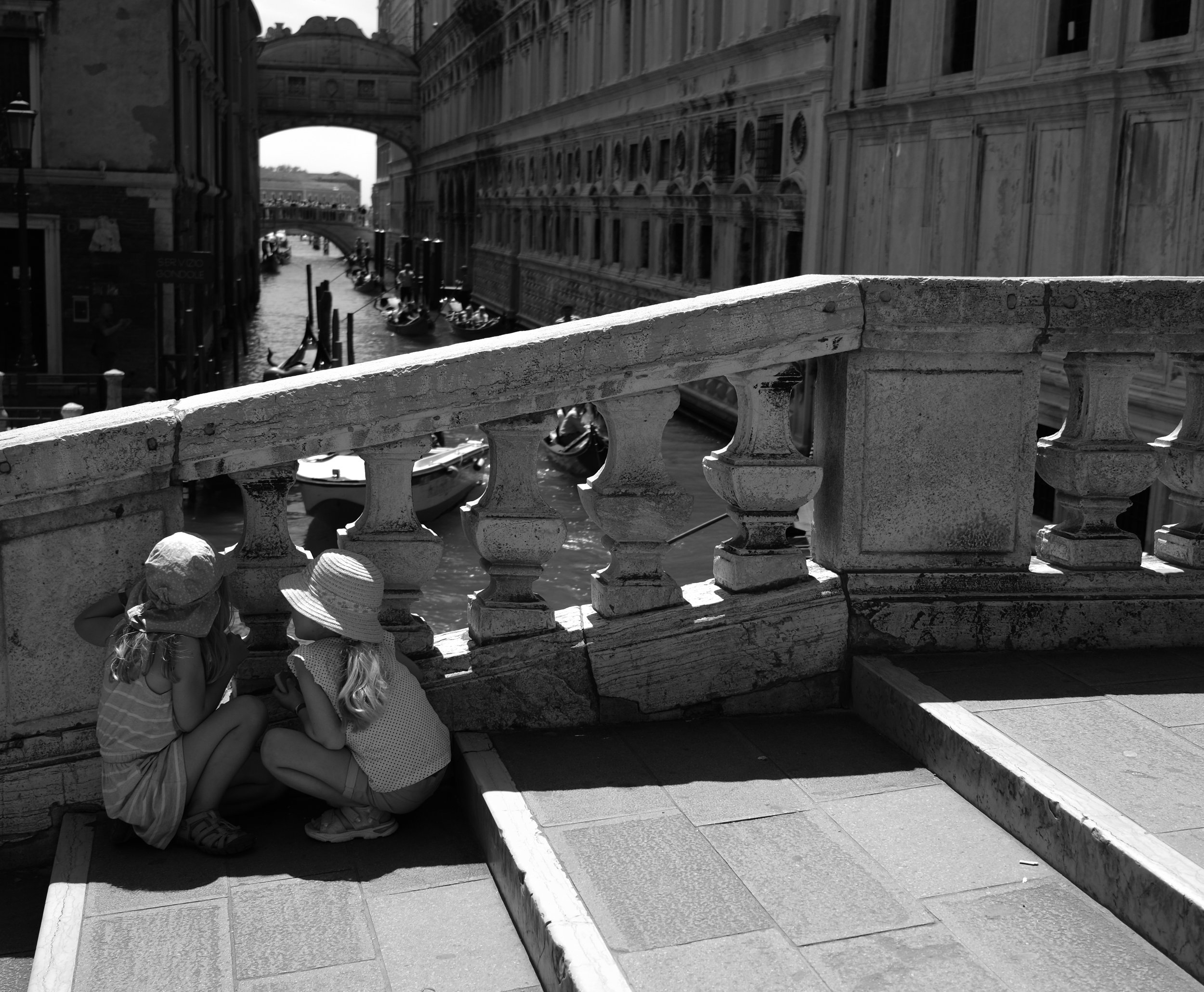 two sisters crouched together on a bridge, watching the gondolas. siblings shape our experiences, and consequently, our world.