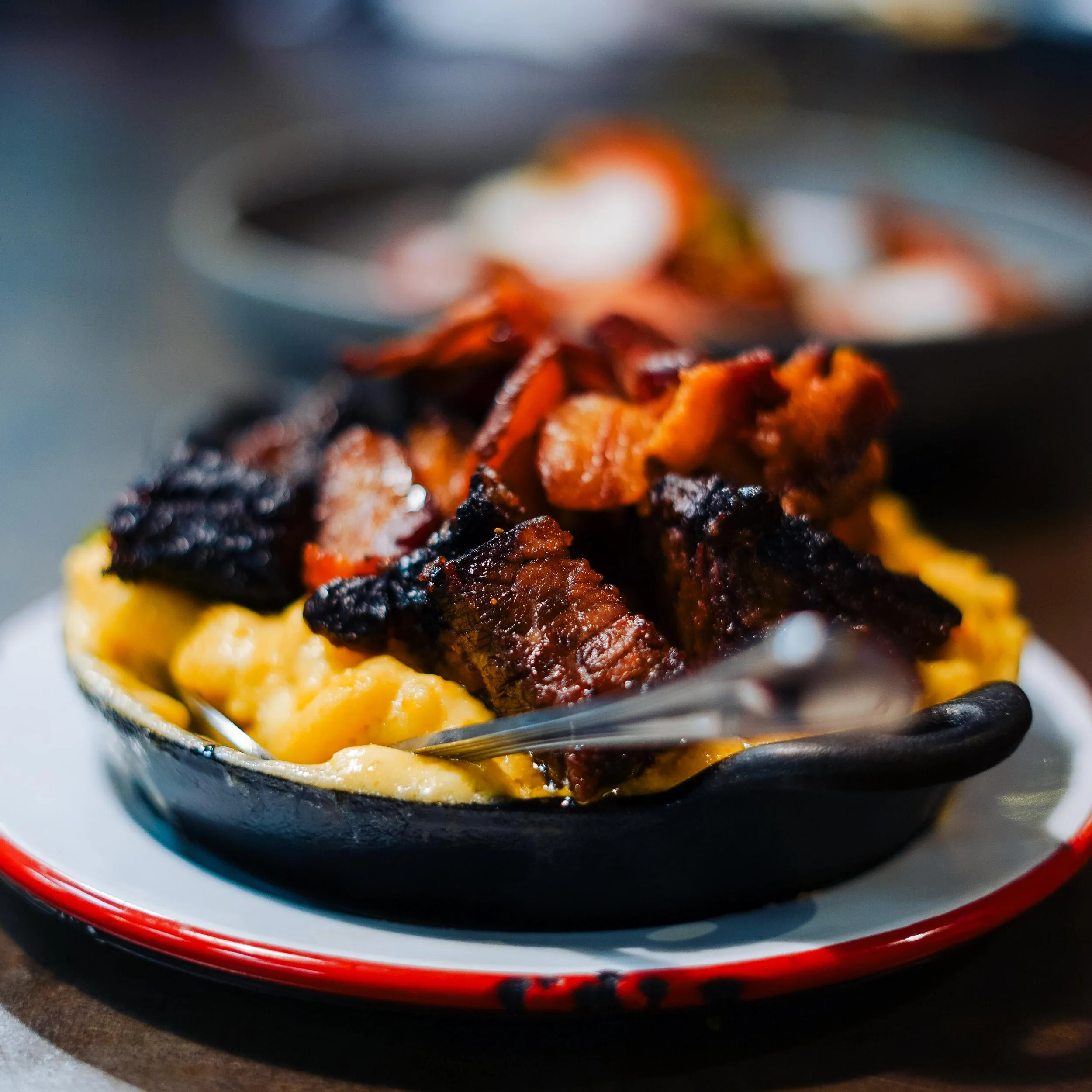 Close-up of a dessert with caramelized toppings on a piece of cake or pastry in a black bowl with a red and white rim.