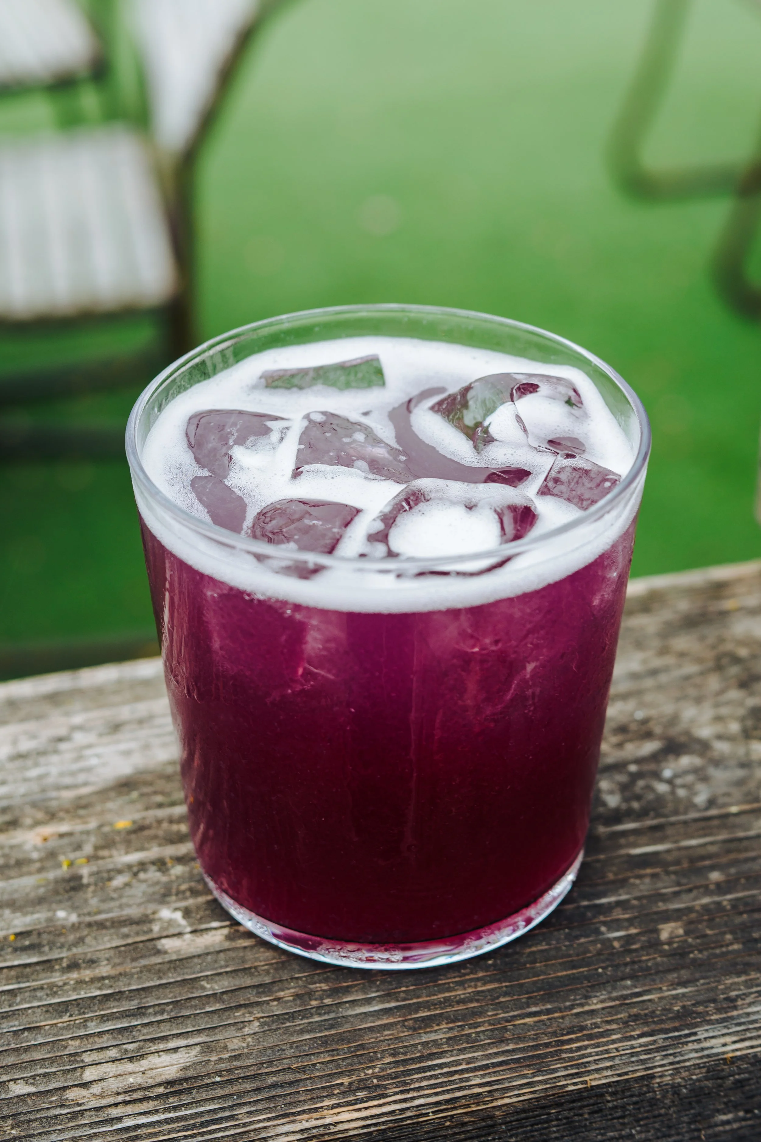 A glass of purple beverage with ice cubes on a wooden surface