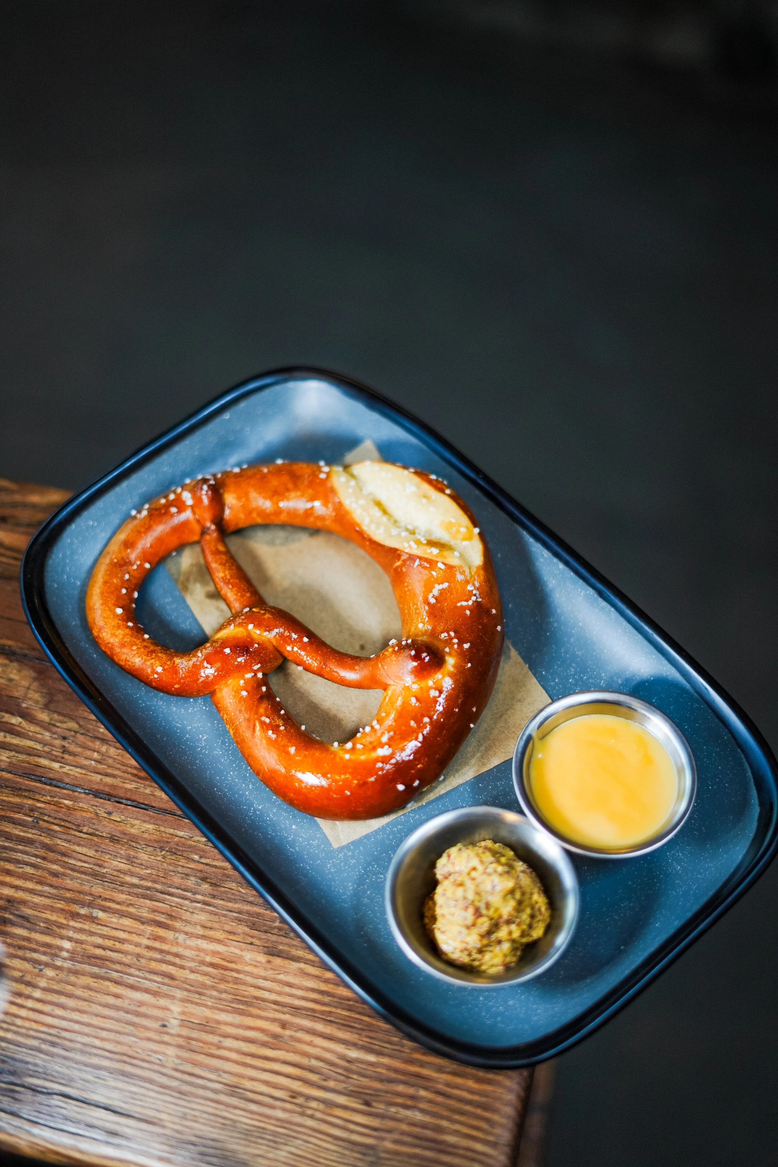 Pretzel with salt served with mustard and cheese dips on a black tray