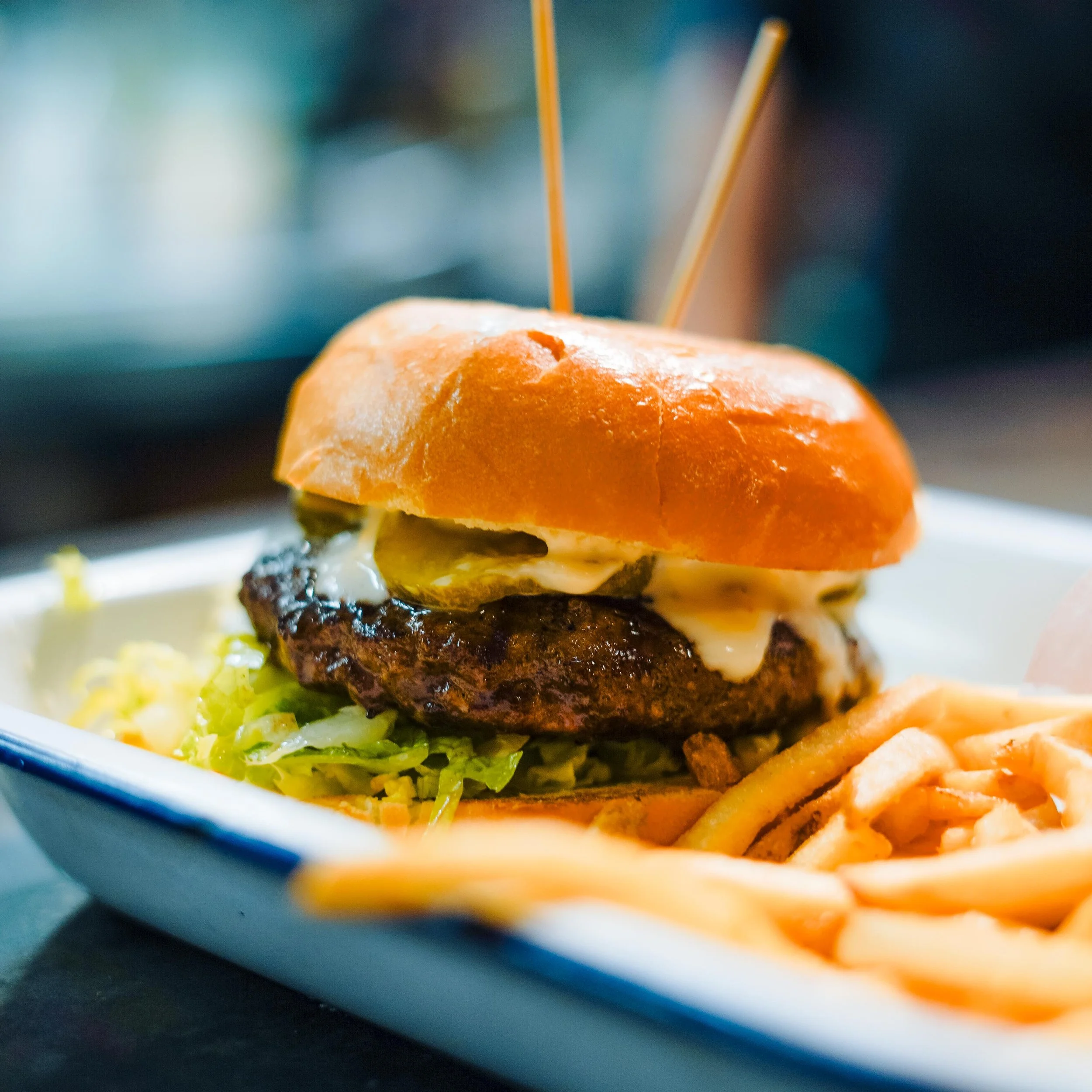Close-up of a gourmet burger with melted cheese, lettuce, tomato, and a toasted bun, served on a white plate.