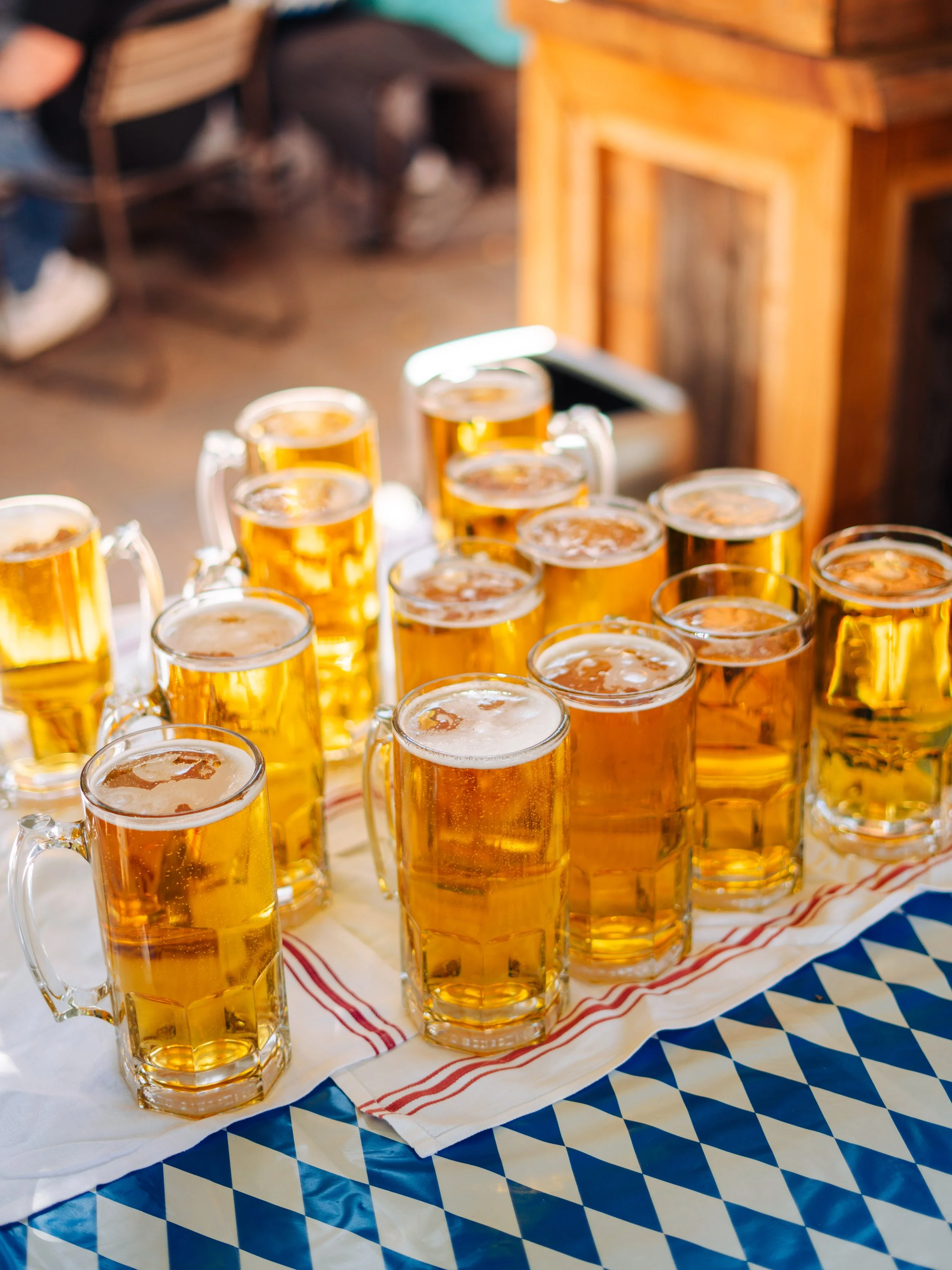 Several glasses of beer arranged on a table with a blue and white checkered tablecloth and a red and white striped cloth underneath.
