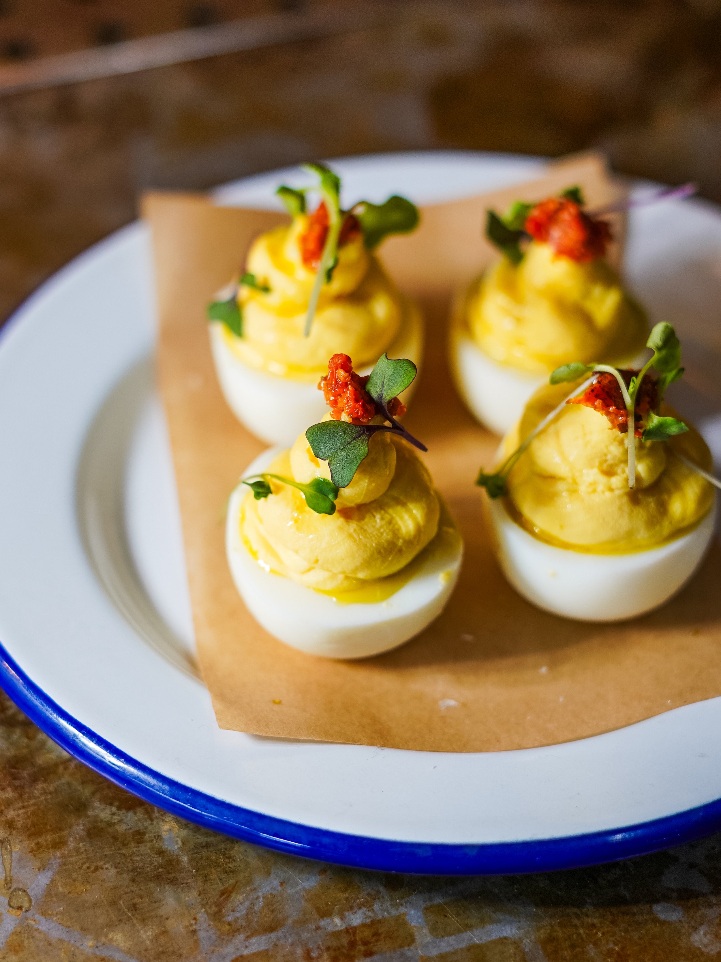 Deviled eggs topped with microgreens and red seasoning served on a white and blue plate