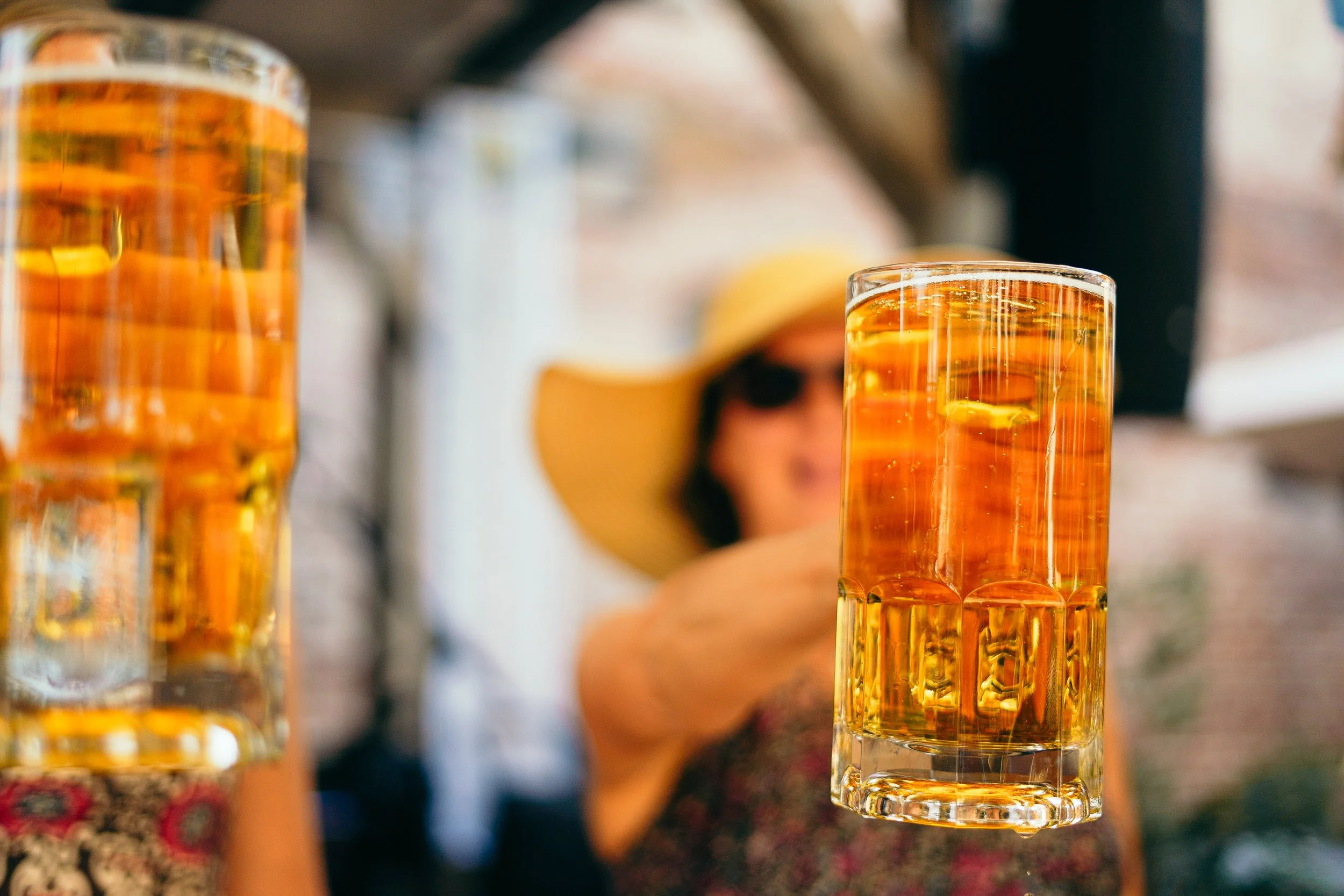 Close-up of a glass filled with amber-colored beer with ice, held by a person, with other glasses of beer in the background.