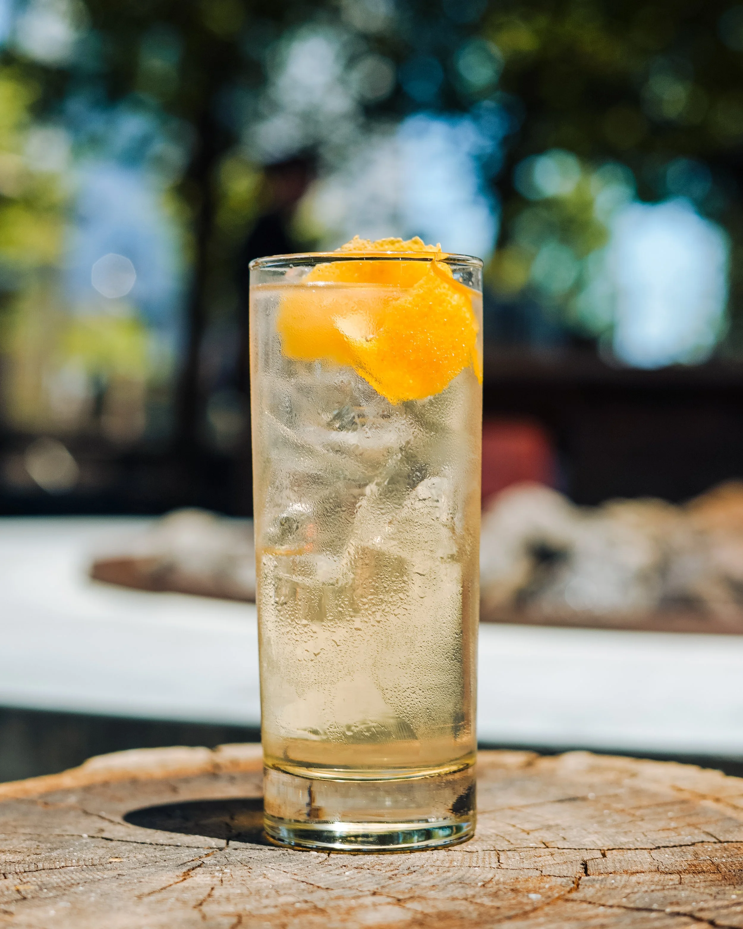 A tall glass of lemonade with ice and a lemon slice on top, placed on a wooden surface outdoors.