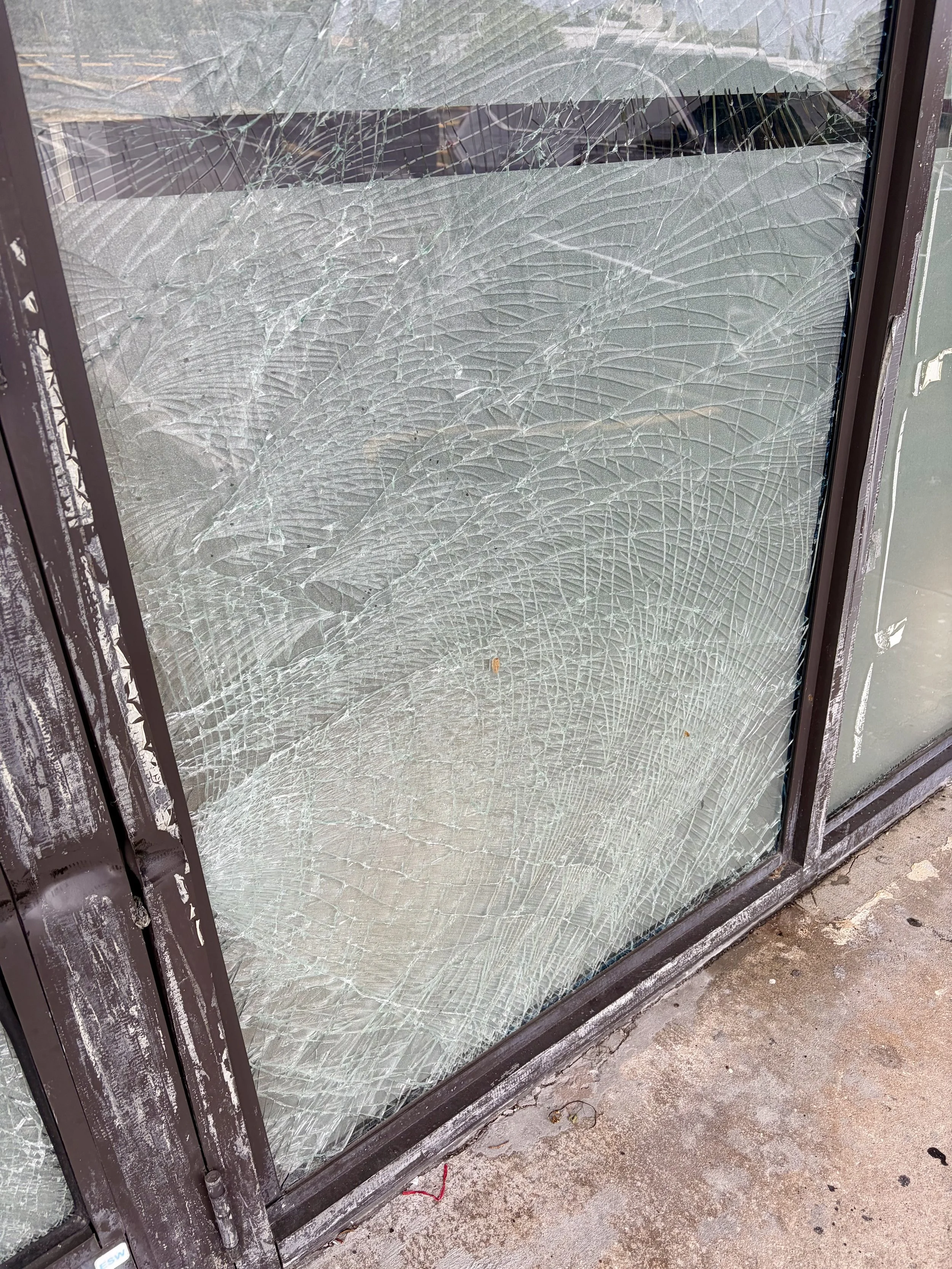 Shattered glass entrance door with extensive cracking while the glass remains in its frame.