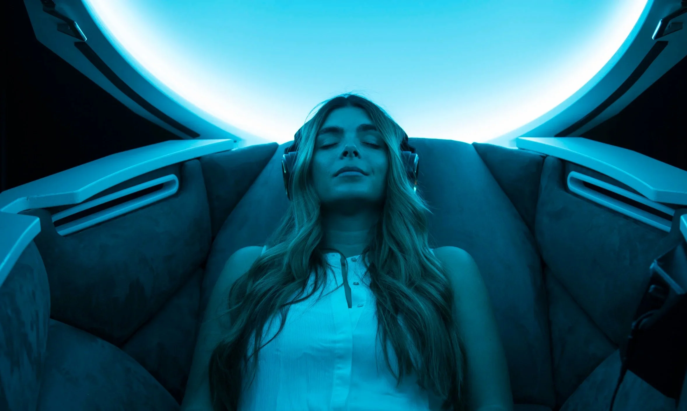 Woman in the Somadome wearing headphones. Calming blue light glows inside the dome.