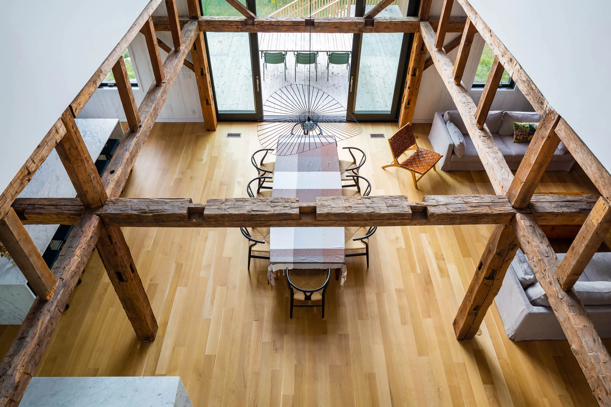 Dining room of a chalet with large windows. Old wooden structure apparent. White oak floor. Vertigo luminaire above the table, Wishbone Chair CH24