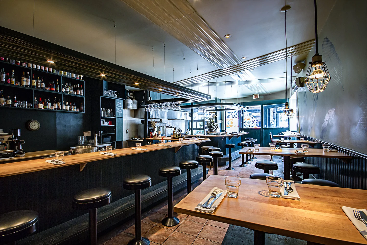 Vue intérieure du restaurant avec son bar fini bois fait en 2 sections et une partie de la salle à manger. Moulures décoratives finies lustrées suspendues au-dessus du comptoir avec éclairage intégré