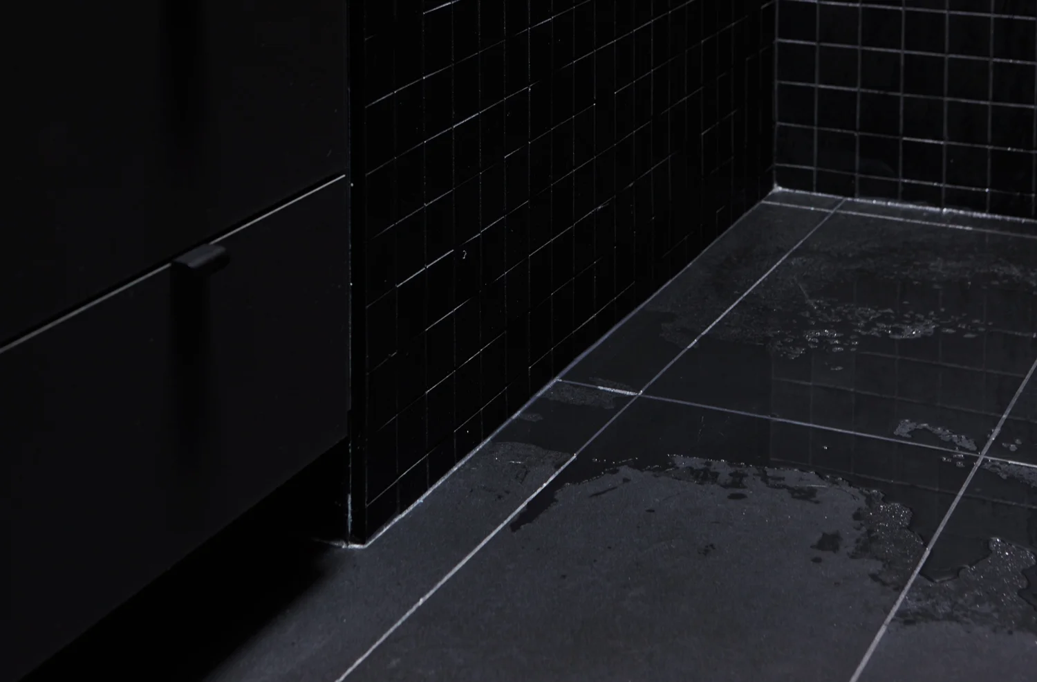 View of the corner of the bathroom. Black ceramic floor with black 2x2 mosaic on the wall. Black washbasin cabinet.