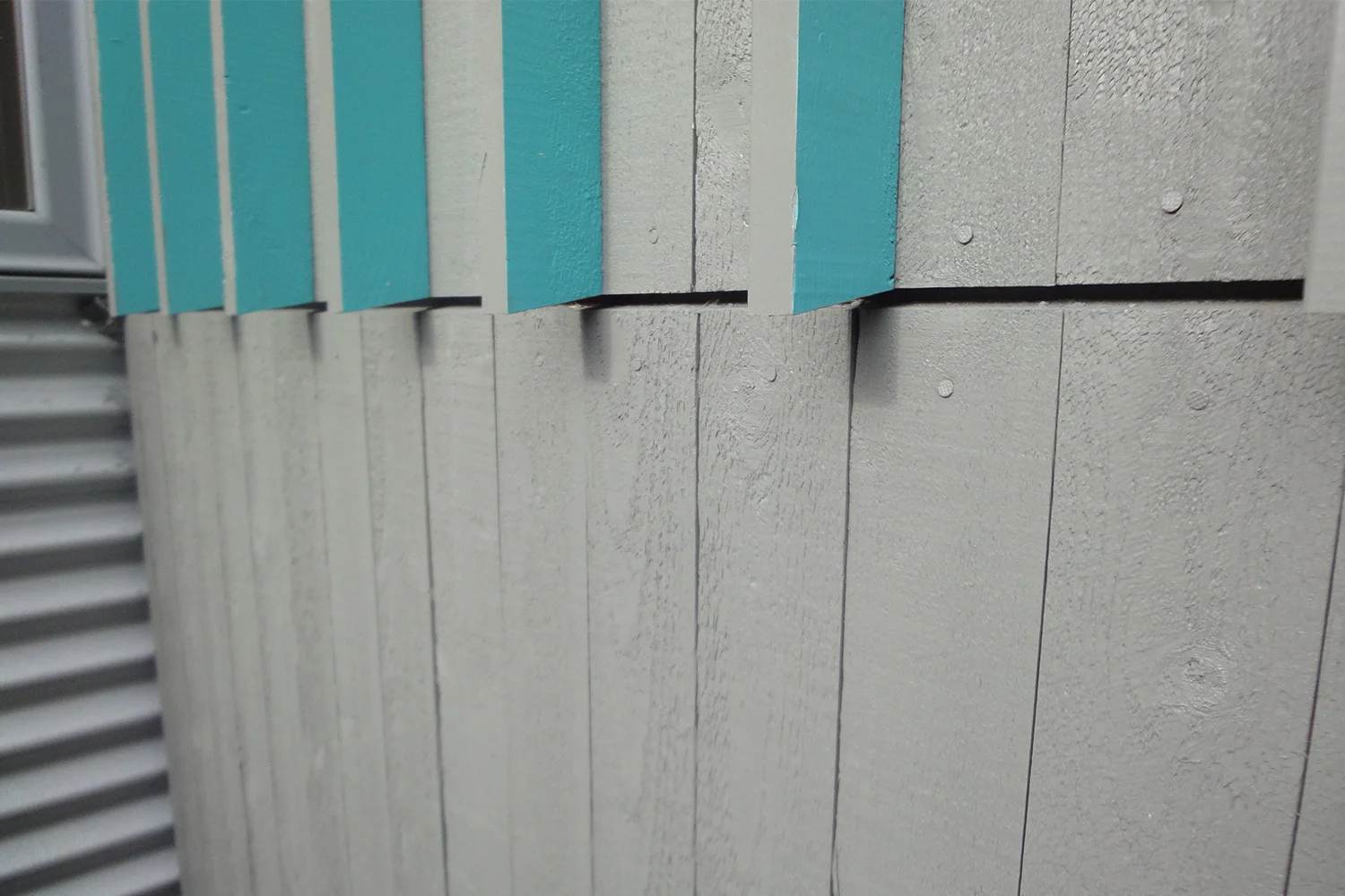 Exterior facade, gray wood siding. Board and batten modern. Turquoise blue painted sticks on one side